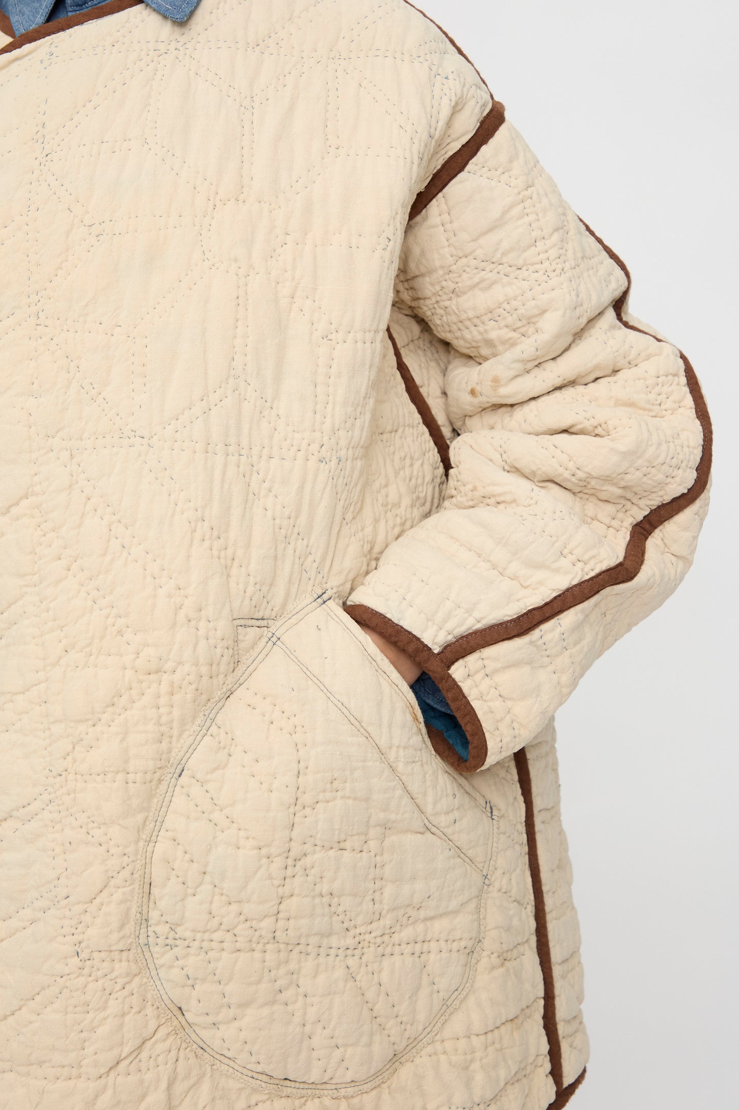 A close-up of a person wearing the As Ever Vintage Quilt Coat in indigo, brown, and yellow features a large front pocket and blue cuff detail.