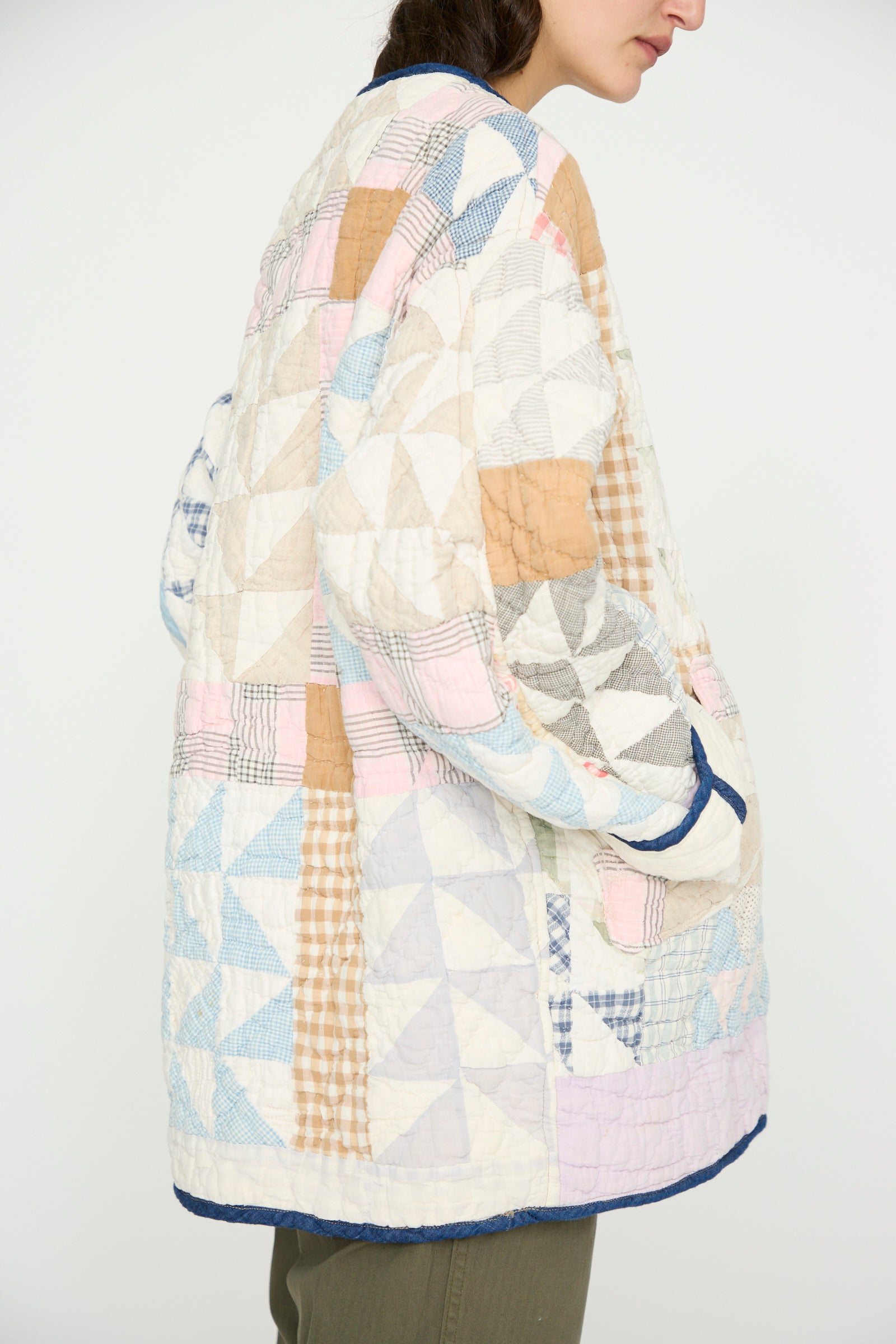 A person wears the As Ever Vintage Quilt Coat in Multi Color, made from vintage cotton with triangle and plaid patterns in pastel tones, standing sideways against a plain background.