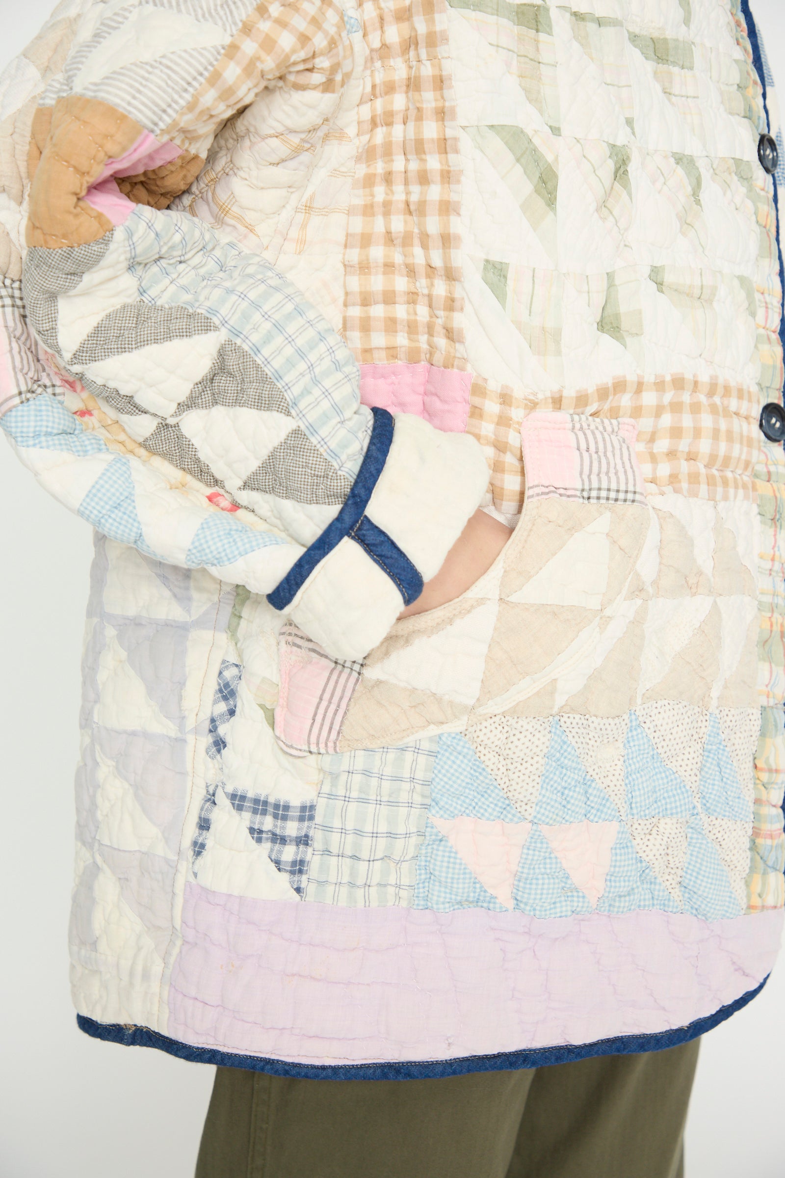 Close-up of a person wearing the 'Vintage Quilt Coat in Multi Color' by As Ever, featuring reversible patchwork made from vintage cotton in various pastel patterns, with a hand tucked into a front pocket.