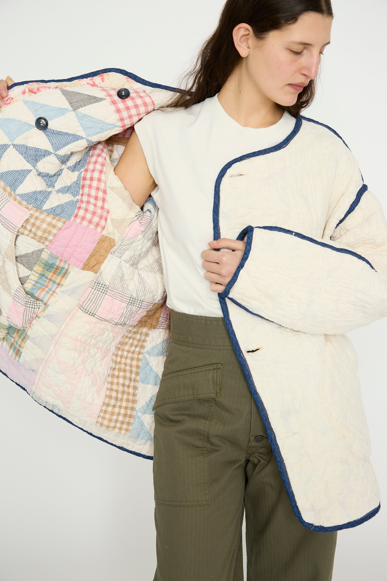 A model in a white t-shirt and olive green pants showcases the Vintage Quilt Coat in Multi Color by As Ever, featuring a reversible design with vintage cotton patchwork lining, against a plain backdrop. 