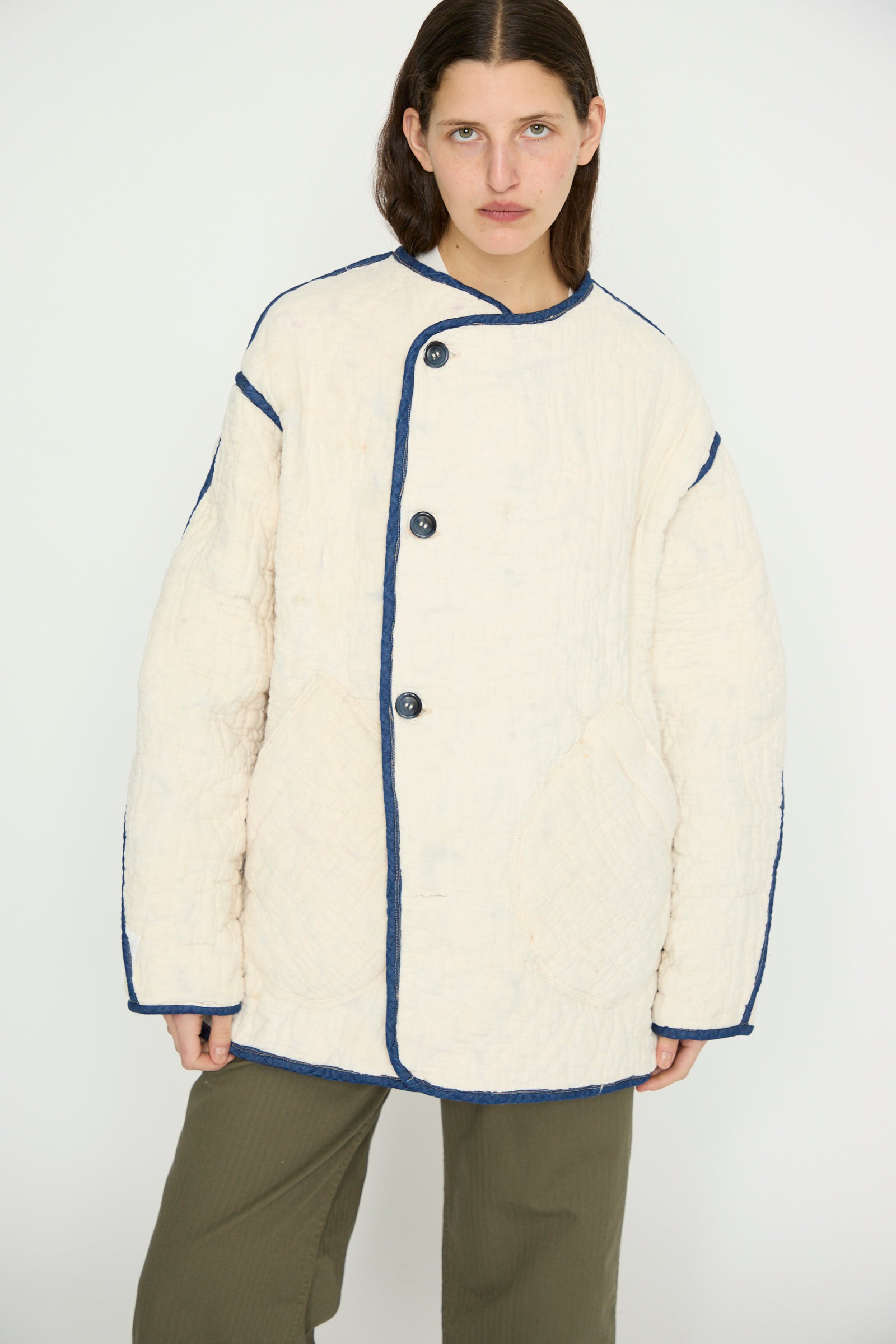 A person wears the As Ever Vintage Quilt Coat in Multi Color, a cream oversized jacket with navy trim, paired with olive pants against a plain background.