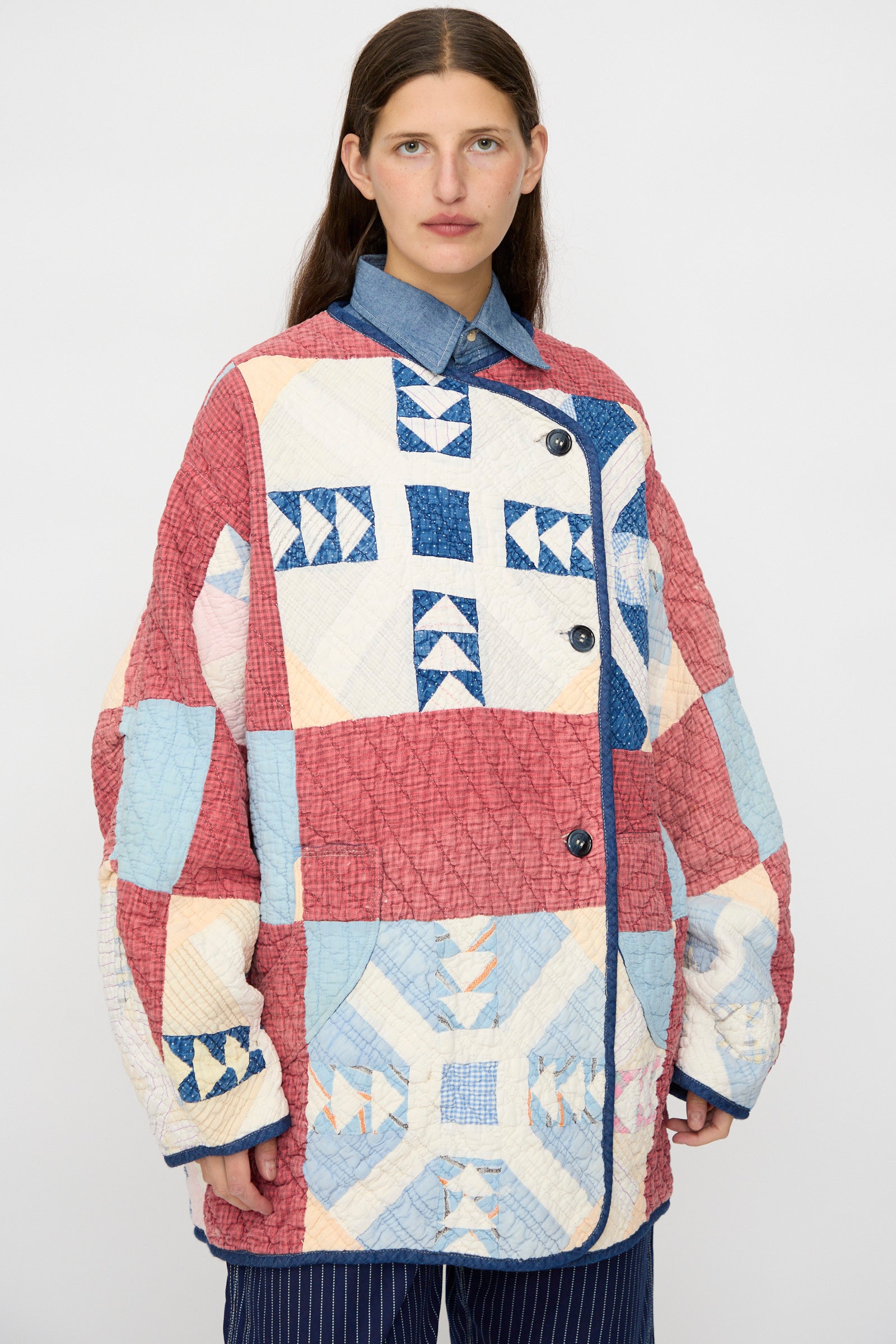 A woman wears the As Ever Vintage Quilt Coat in Red and Blue, featuring geometric patterns, as she stands facing forward against a plain background.