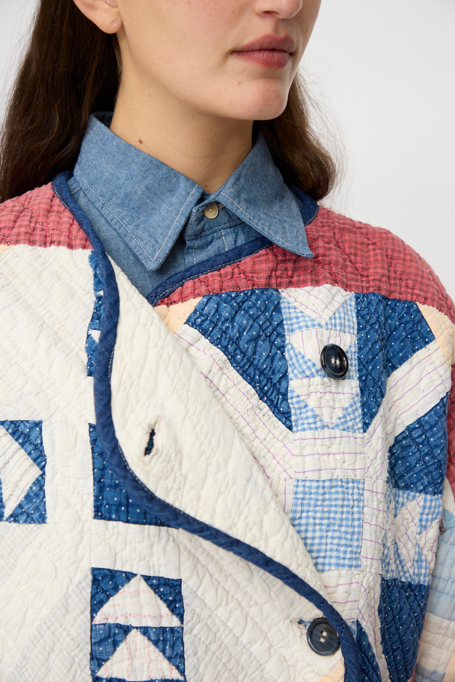 A person wearing a blue chambray button-up shirt under the As Ever Vintage Quilt Coat in Red and Blue.