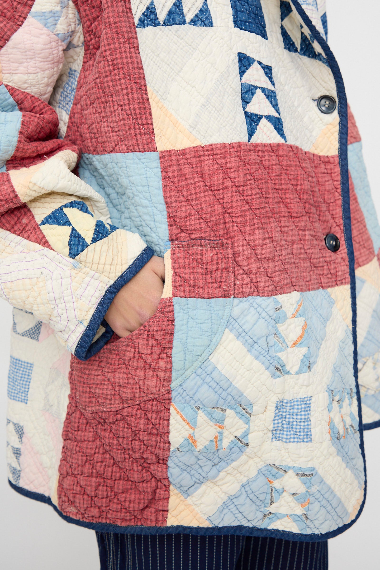 Someone wearing the As Ever Vintage Quilt Coat in Red and Blue, featuring red, blue, and cream geometric patterns, has their hand in the side pocket.