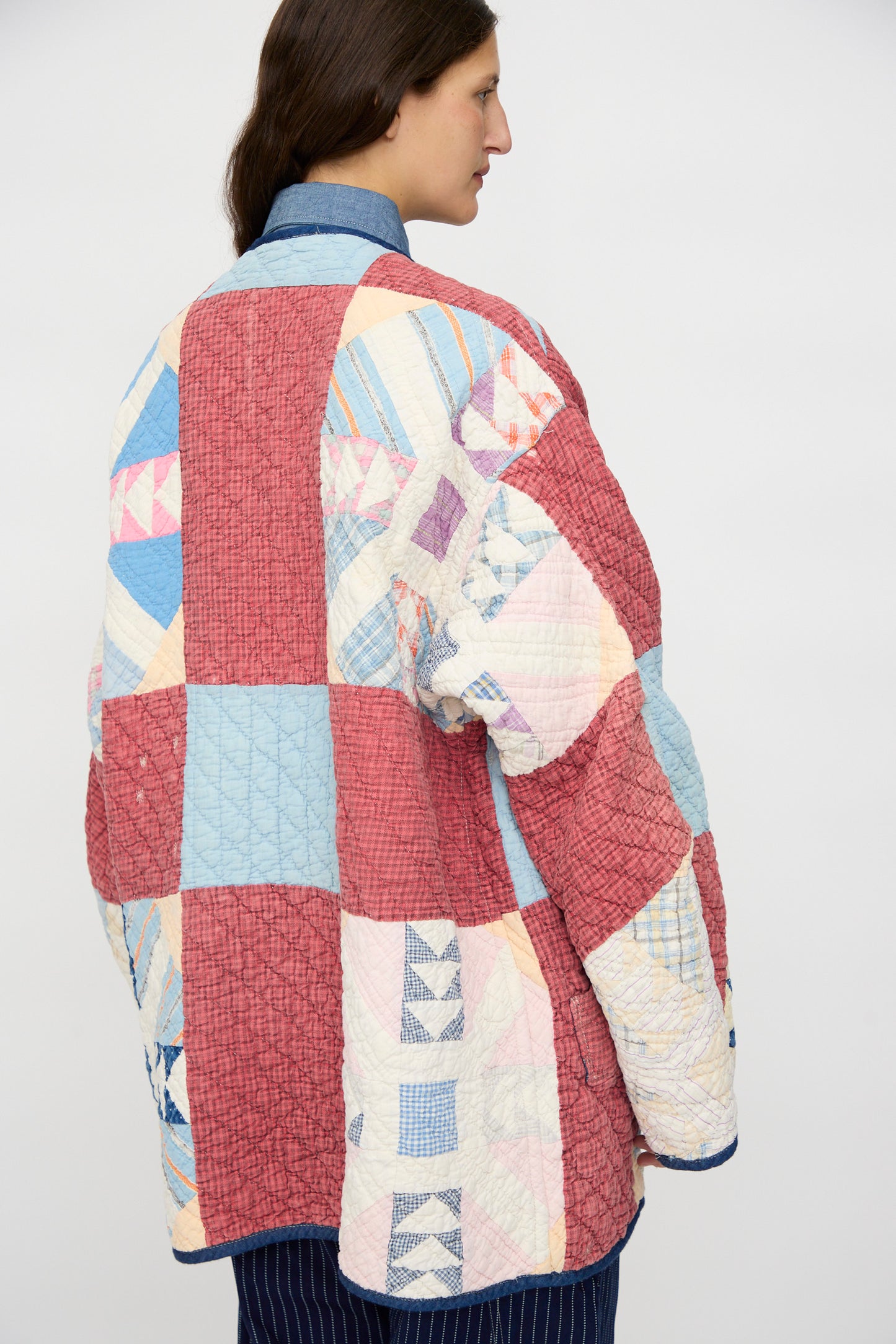 Wearing the As Ever Vintage Quilt Coat in Red and Blue, featuring hand-sewn red, blue, and cream squares, the person stands with their back to the camera against a plain background.