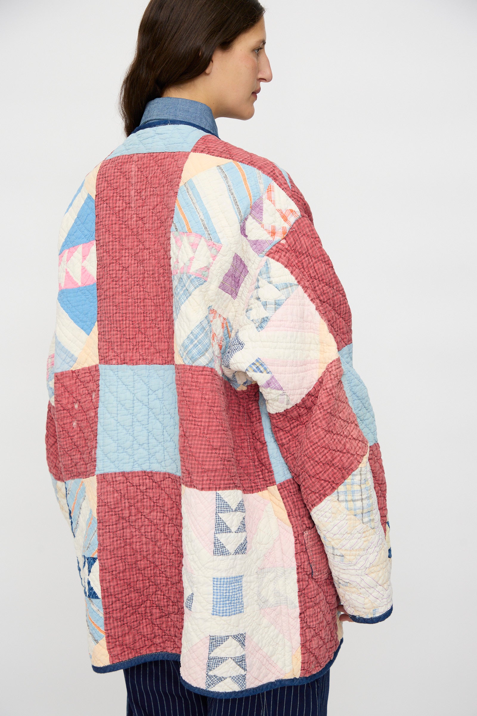 Wearing the As Ever Vintage Quilt Coat in Red and Blue, featuring hand-sewn red, blue, and cream squares, the person stands with their back to the camera against a plain background.