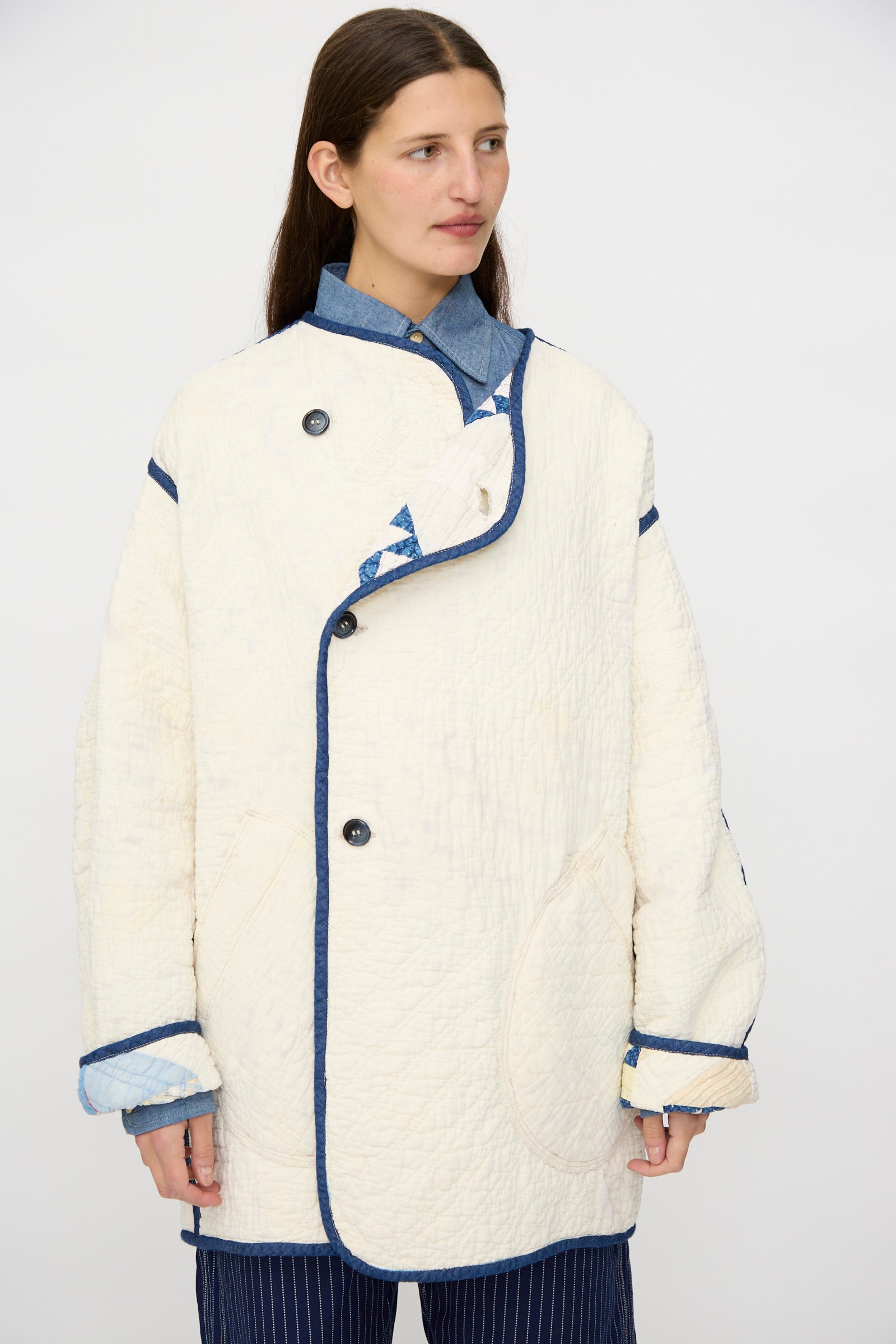 A person wears the As Ever Vintage Quilt Coat in Red and Blue over a blue collared shirt and pinstriped pants, standing against a plain light background.