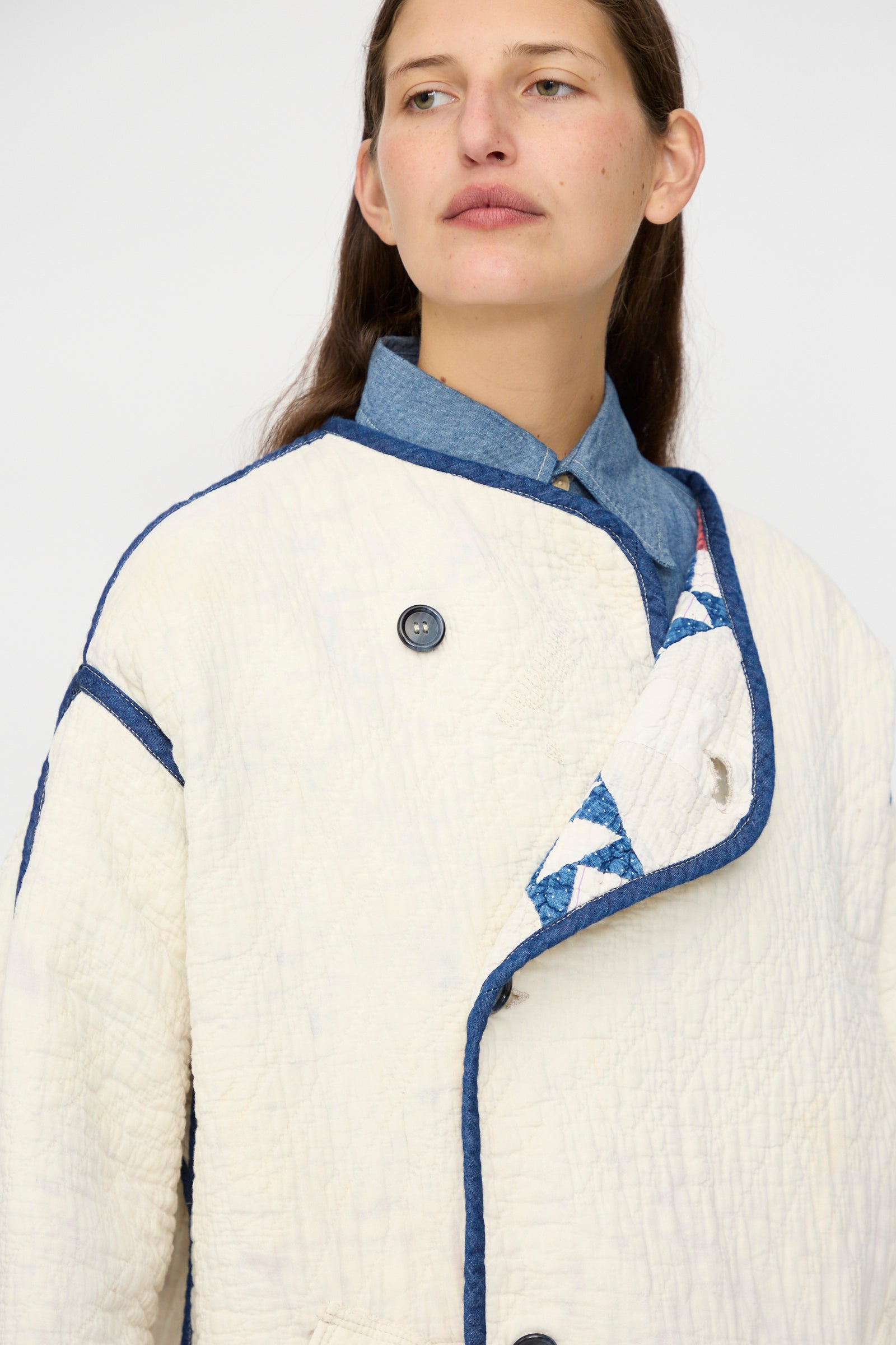 A person wears the As Ever Vintage Quilt Coat in Red and Blue over a denim shirt, glancing to the side against a plain background.