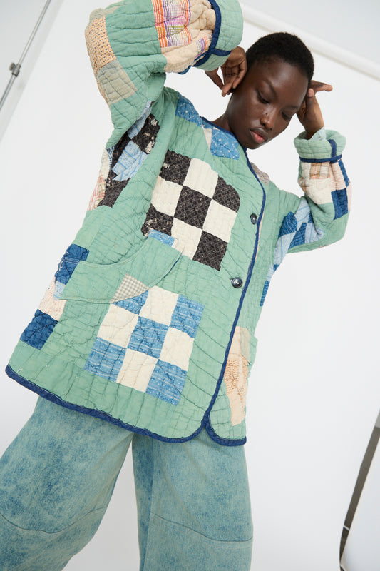 A model stands with eyes closed and hands near their head, wearing an oversized Vintage Quilt Jacket in Green Multi by As Ever, featuring a patchwork pattern.