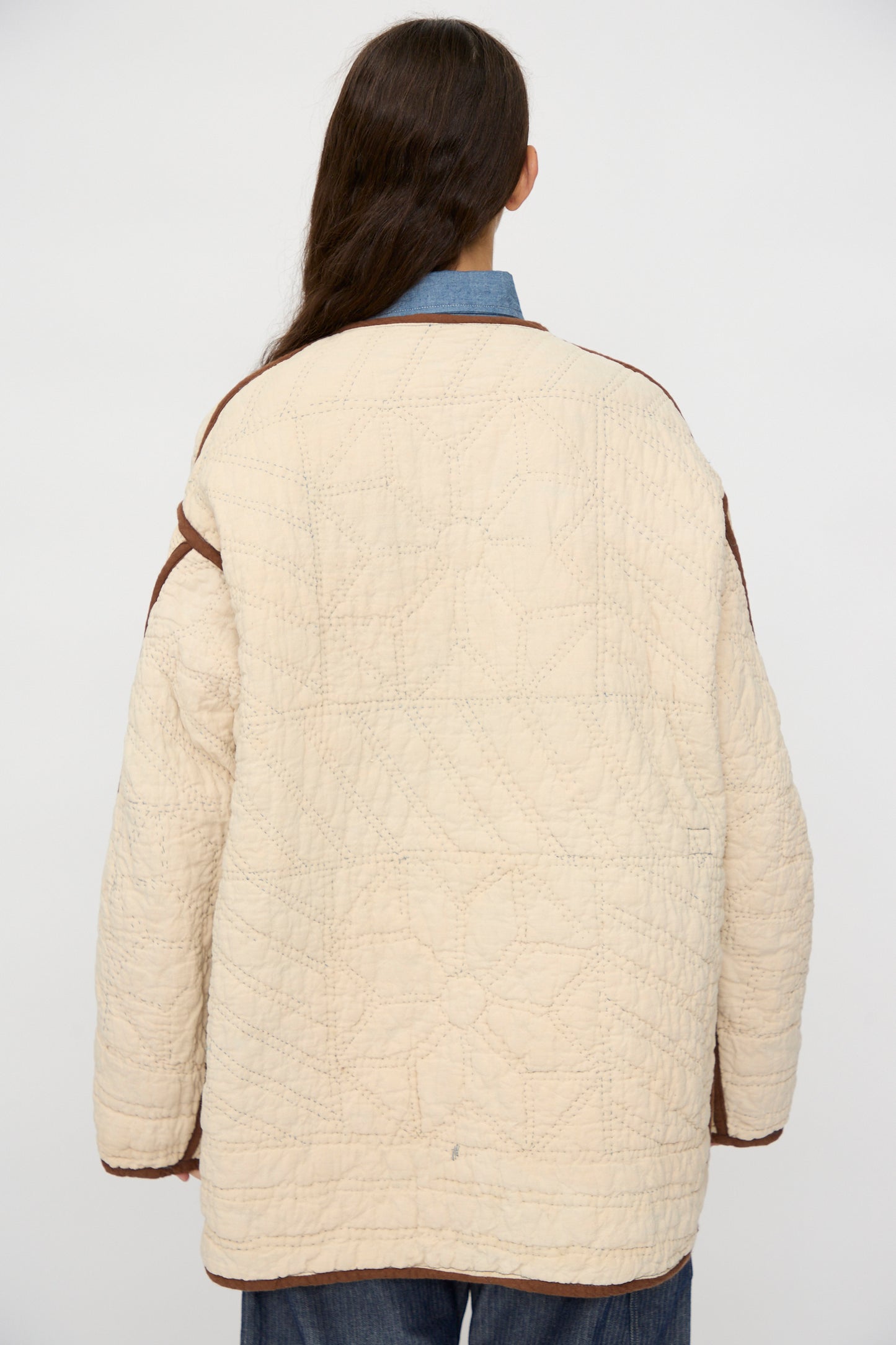 A person with long brown hair faces away from the camera, wearing the As Ever Vintage Quilt Coat in Indigo, Brown and Yellow against a plain background.