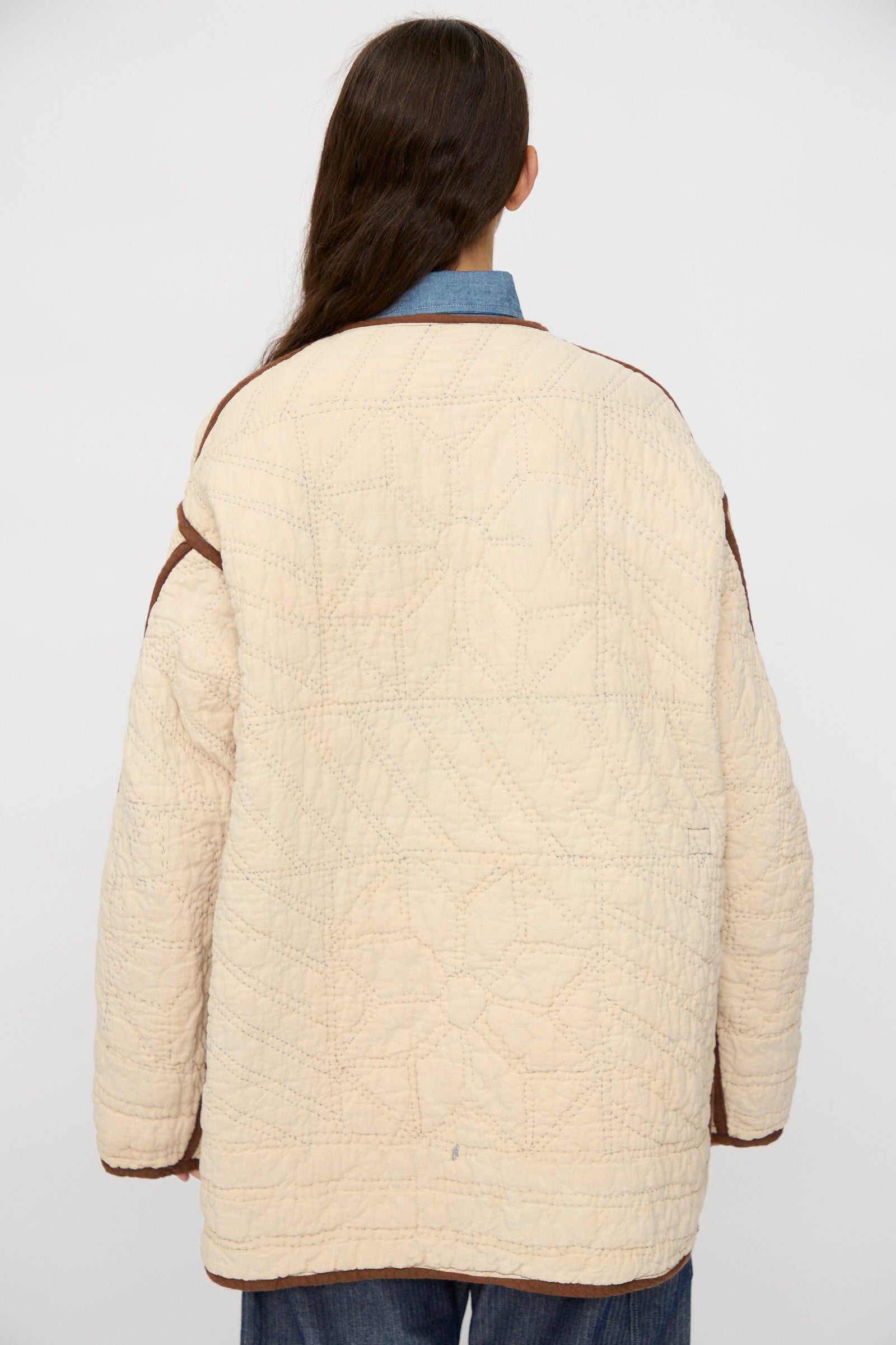 A person with long brown hair faces away from the camera, wearing the As Ever Vintage Quilt Coat in Indigo, Brown and Yellow against a plain background.