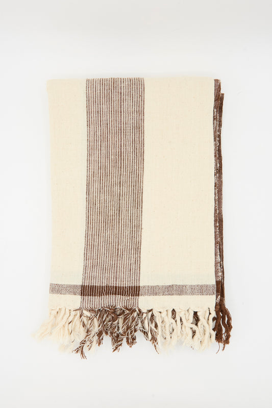 The Auntie Oti Cotton Khadi Natural Dye Towel in Brown Stripe features cream-colored cotton with brown stripes and fringed edges, displayed on a plain white background.