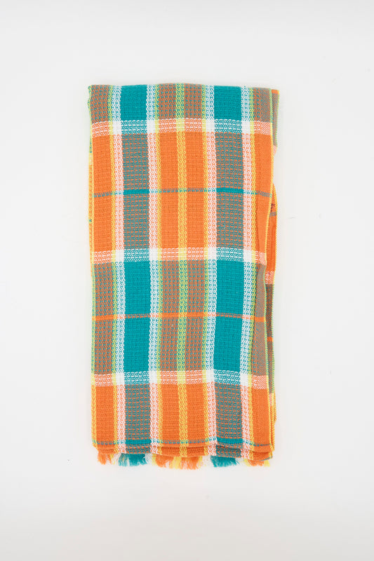 The Auntie Oti Dobby Plaid Towel in Orange and Green is a handwoven rectangular kitchen towel with short tasseled edges and a check plaid pattern, shown folded against a plain white background.
