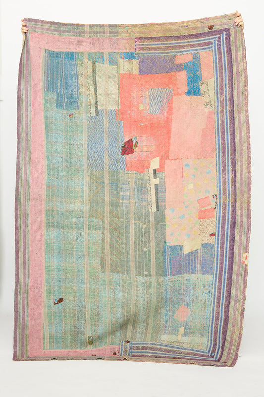 A person holds up the One of a Kind Vintage Kantha Quilt III by Auntie Oti, a large, hand-stitched patchwork quilt made from upcycled cotton with vertical stripes, pastel tones, and abstract geometric designs.