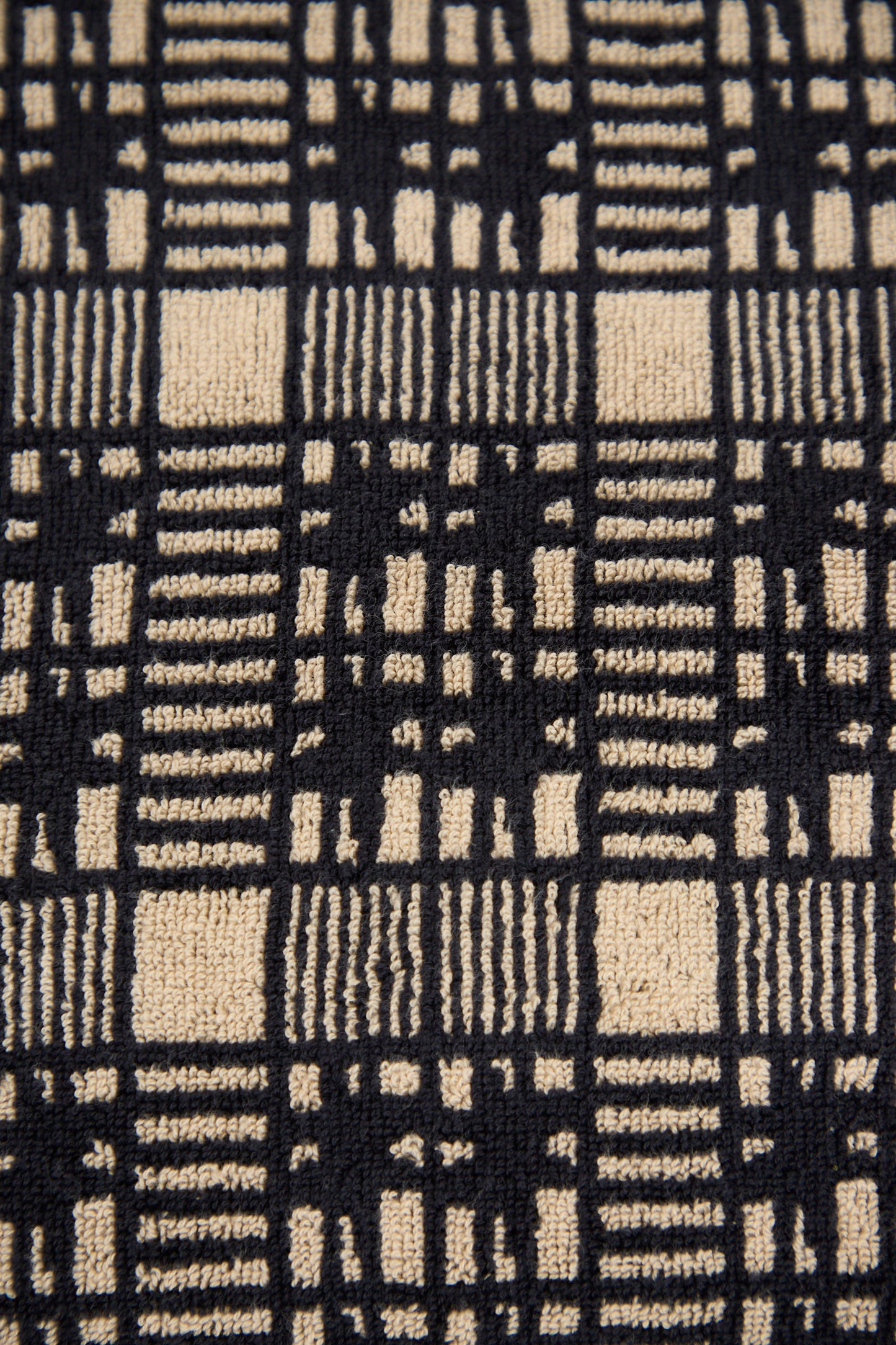 Close-up of the Alma Bath Sheet by Autumn Sonata, showcasing a black and beige checked pattern with vertical and horizontal lines forming a grid-like design.