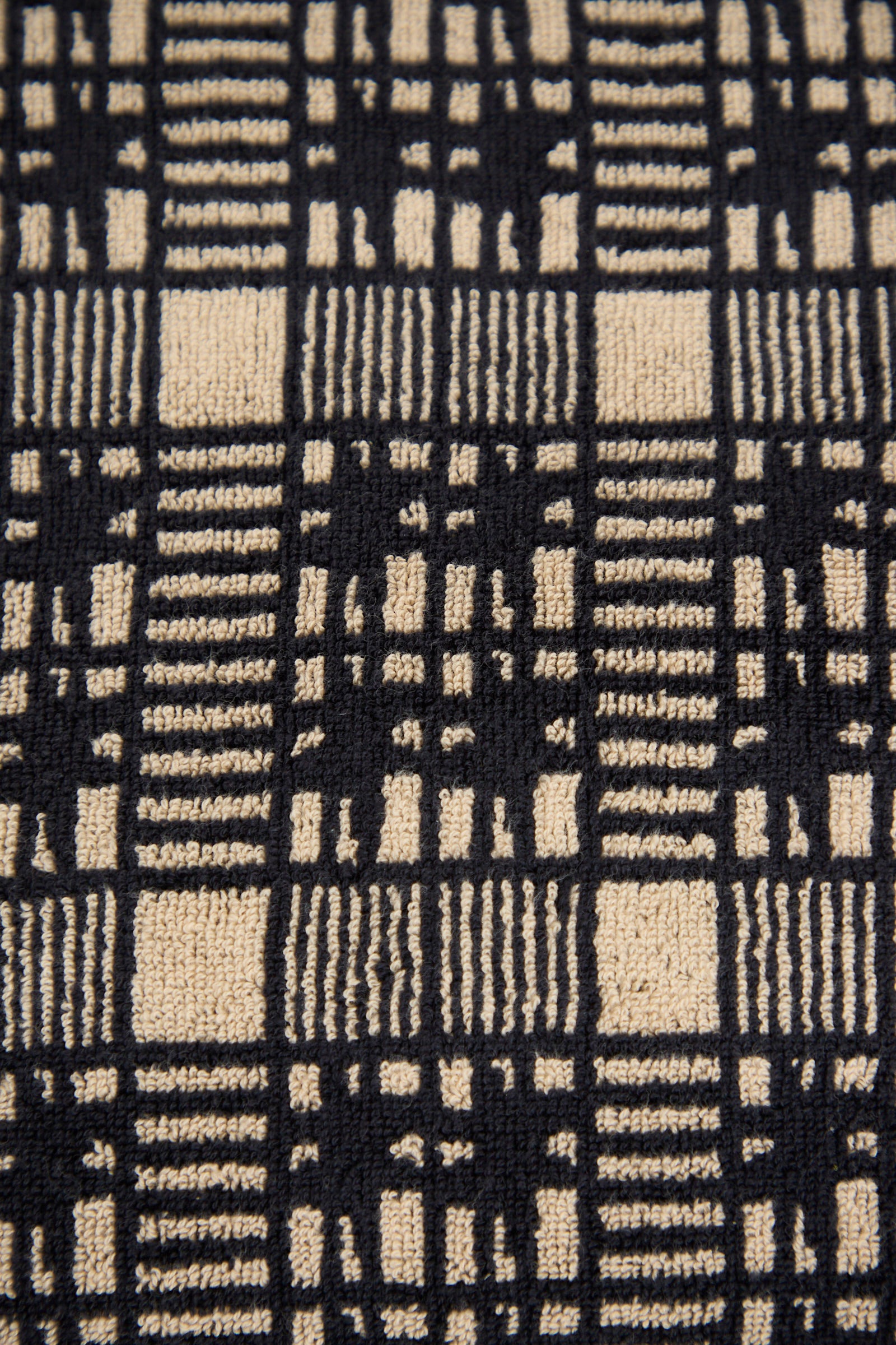Close-up of the Alma Bath Sheet by Autumn Sonata, showcasing a black and beige checked pattern with vertical and horizontal lines forming a grid-like design.