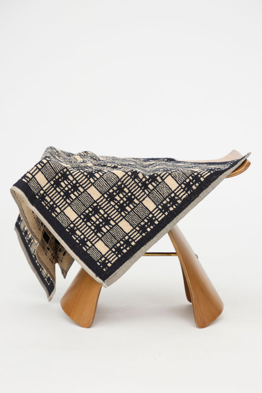 The Alma Hand Towel by Autumn Sonata, crafted from organic cotton and featuring a black and beige geometric pattern, is elegantly draped over a modern wooden stool against a plain white background. This stylish and sustainable piece enhances any space.