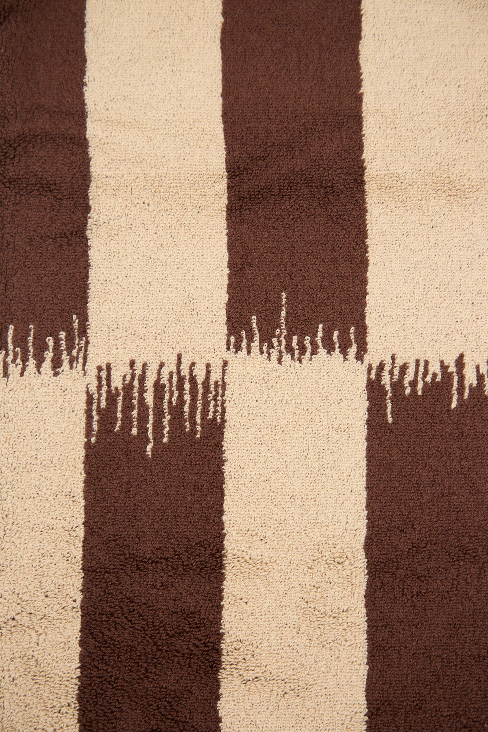 A close-up of the textured organic cotton fabric of the Autumn Sonata Karin Bath Sheet, featuring vertical brown and beige stripes with irregular, jagged edges where the colors meet, reminiscent of traditional Katazome dyeing techniques.