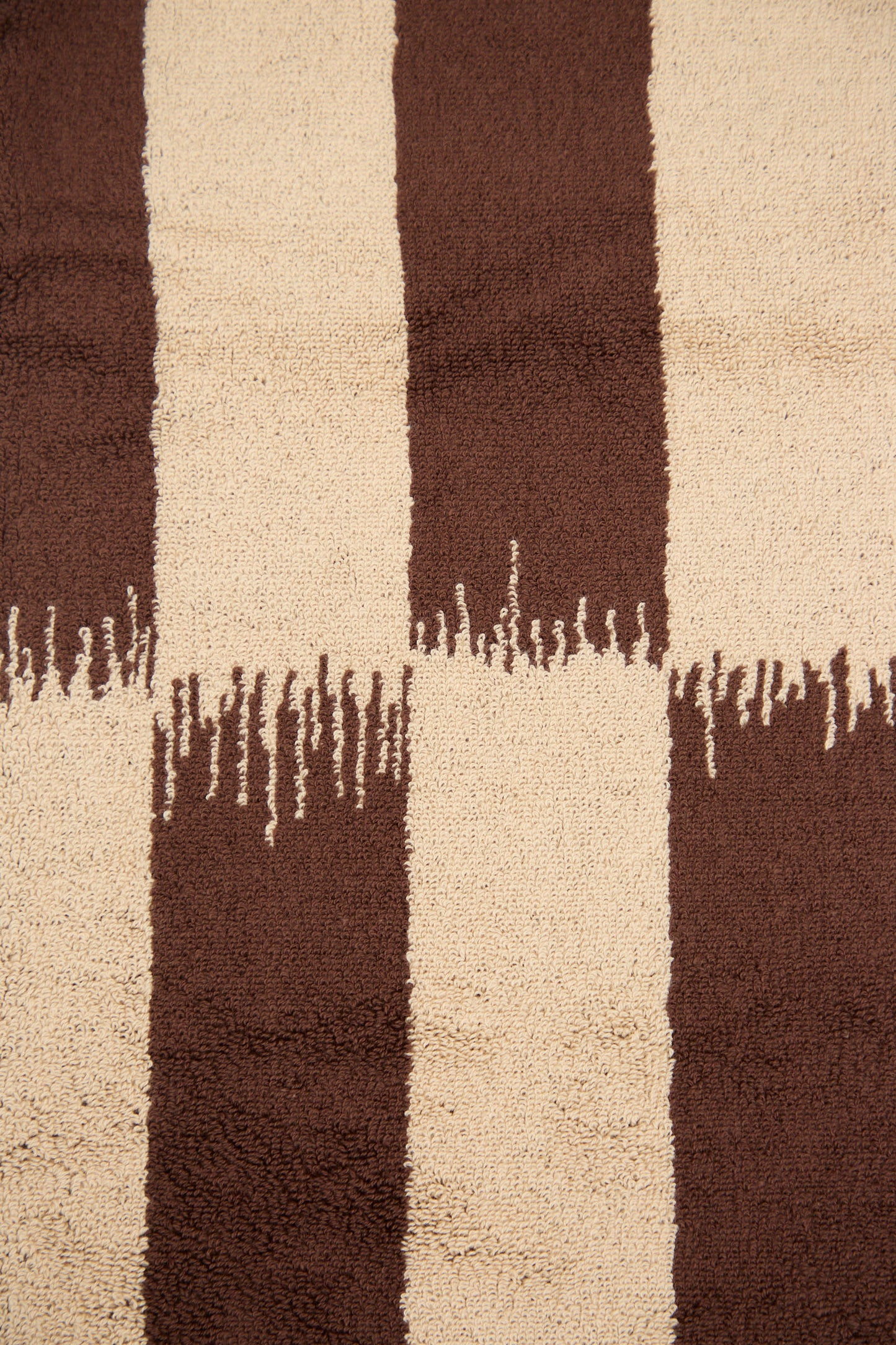 The Karin Hand Towel by Autumn Sonata features a textured fabric with alternating vertical brown and beige stripes, characterized by uneven, jagged edges at each color transition—a nod to the timeless Ikat pattern. Inspired by traditional textile art.