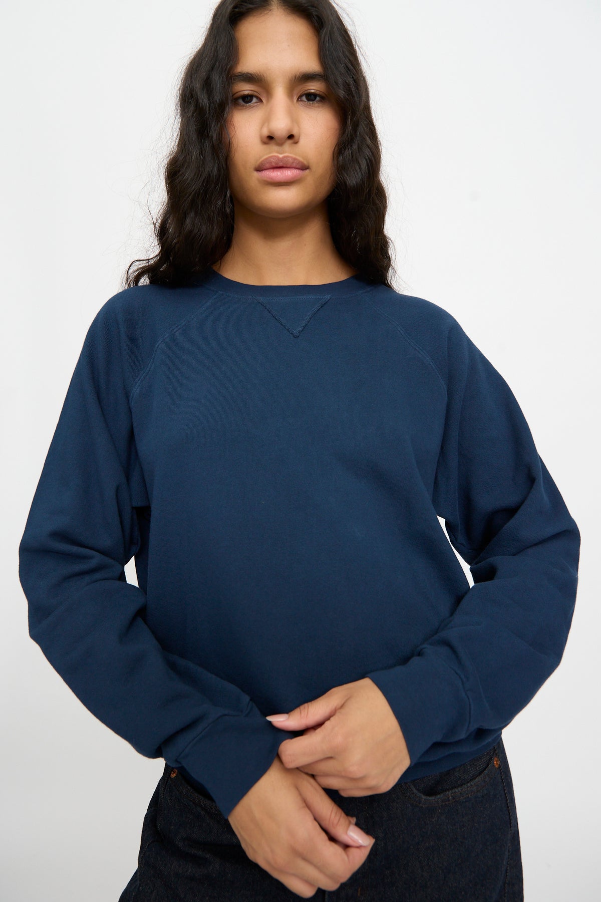 Person with long, wavy hair wears the B Sides Arena Crewneck in Marine Overdye— a relaxed fit, dark blue French terry sweatshirt—against a neutral background.