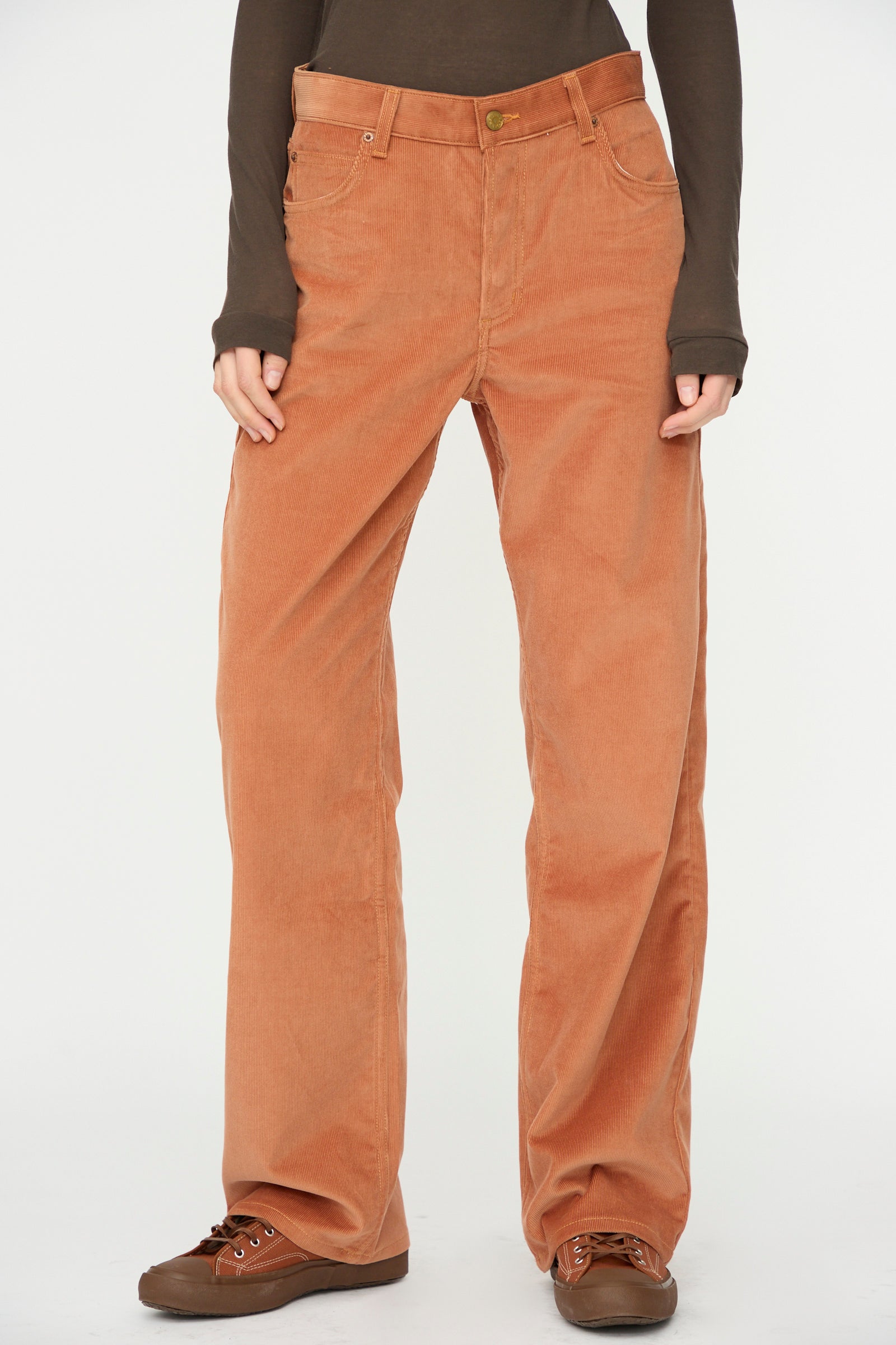 Person wearing B Sides Bec Jean in Peach Tile, styled with a brown long-sleeve shirt and brown shoes, standing against a white background.