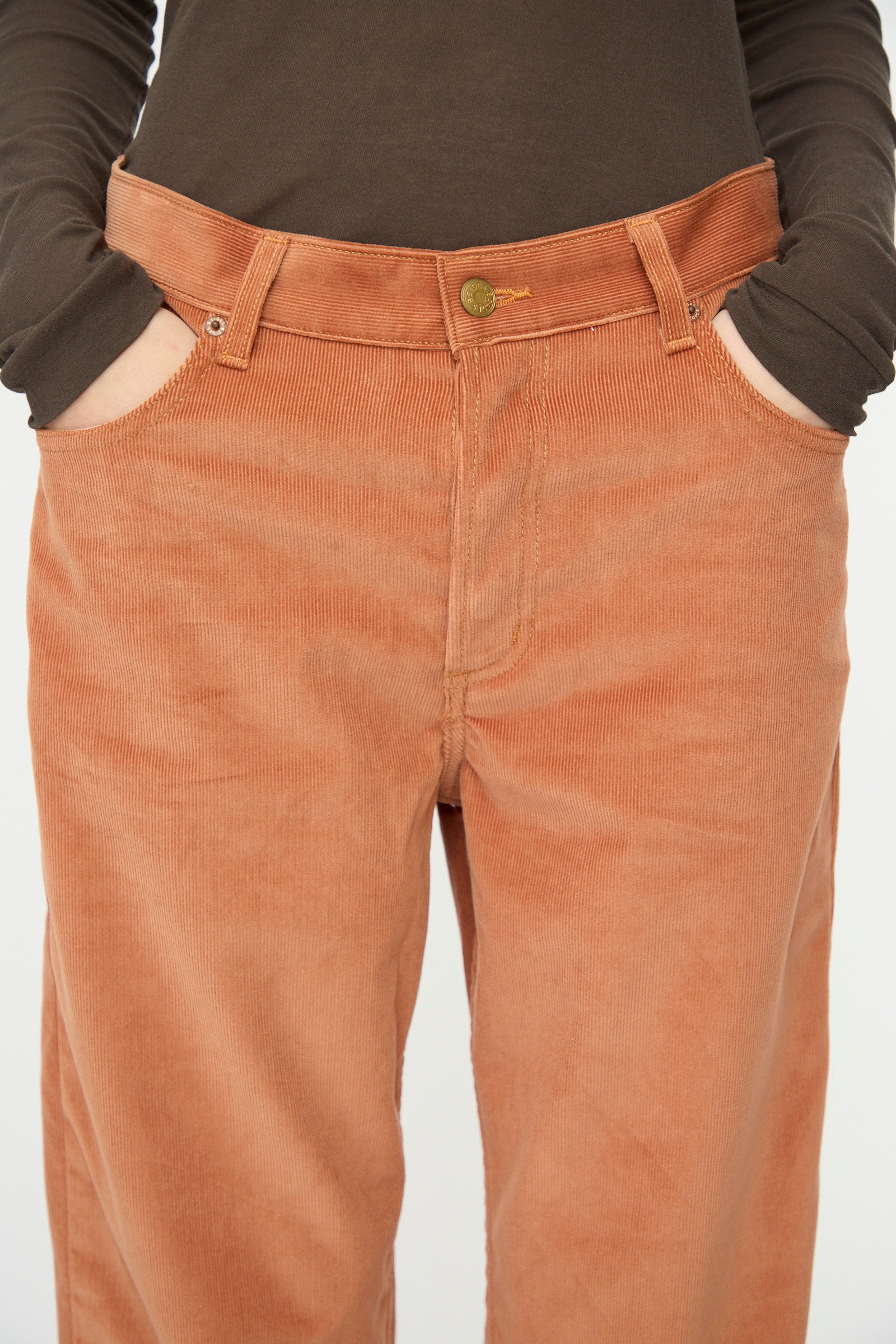 Model wearing B Sides Bec Jean in Peach Tile, a high-waisted, wide-leg velvet corduroy pant with hands in pockets, paired with a brown long-sleeve shirt.