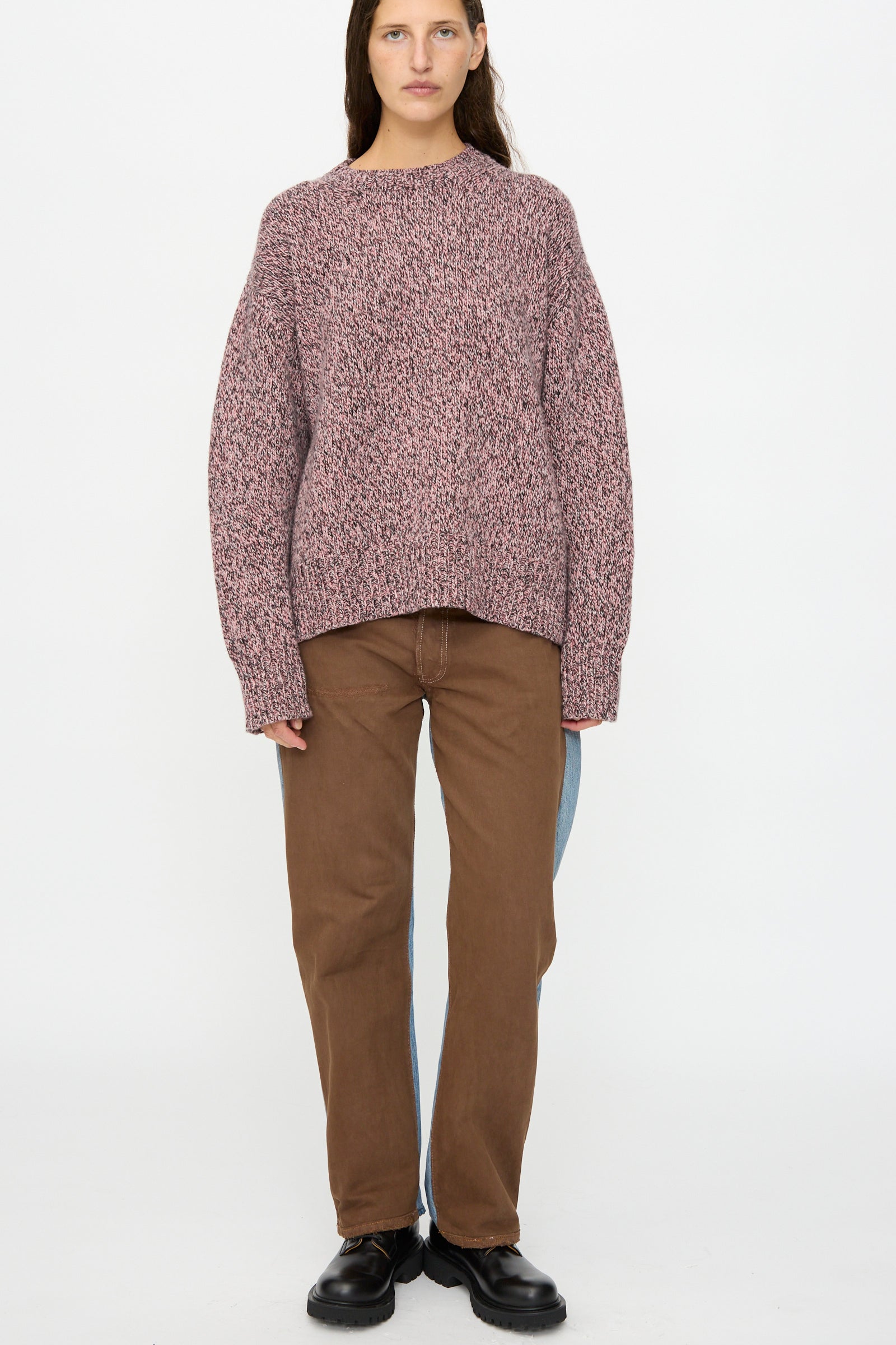 A person stands against a plain background wearing the B Sides Braided Lambswool Crew in Etowah Twist, brown straight-leg pants with a light blue stripe on one leg, and black shoes.