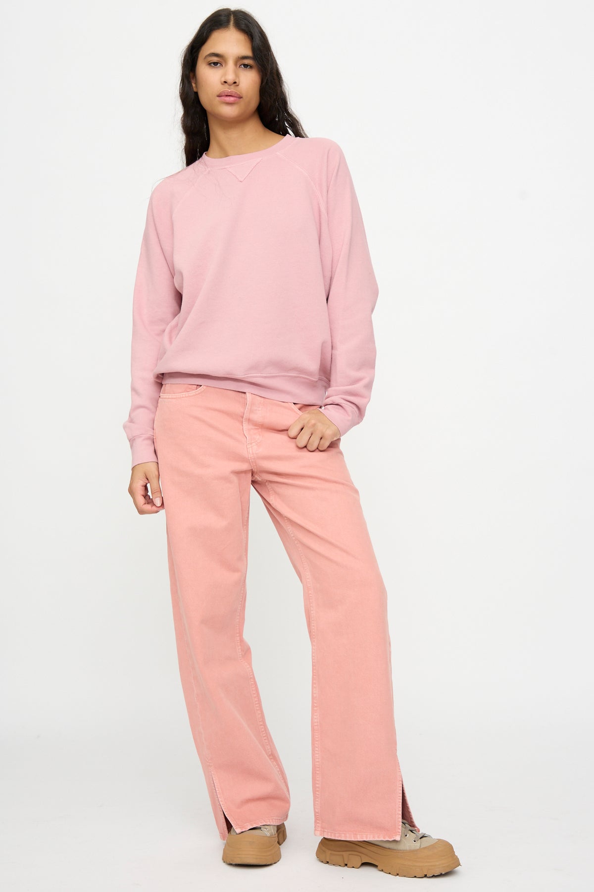 Person standing against a plain background, wearing a pink sweatshirt, tan shoes, and B Sides Charlot Split Hem in Myra Pink Overdye jeans.