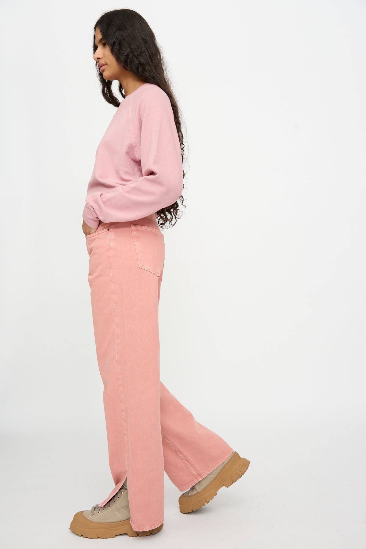 Person standing sideways in a Charlot Split Hem in Myra Pink Overdye by B Sides with relaxed fit jeans and tan shoes against a plain white background.