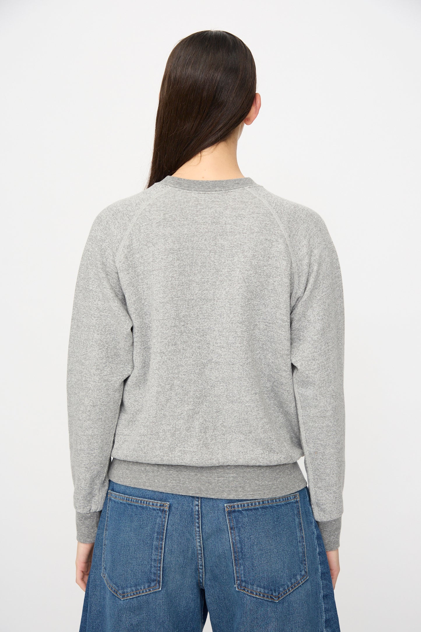 A person stands with their back to the camera in a relaxed fit B Sides Crewneck Sweater in Heather Grey and blue jeans, set against a plain white background.