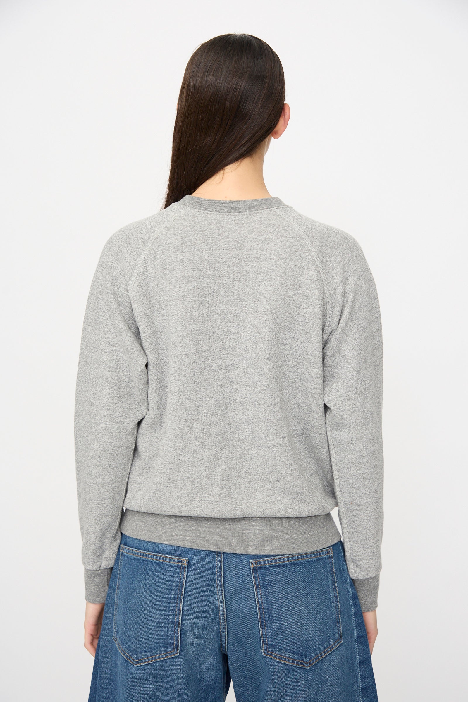 A person stands with their back to the camera in a relaxed fit B Sides Crewneck Sweater in Heather Grey and blue jeans, set against a plain white background.