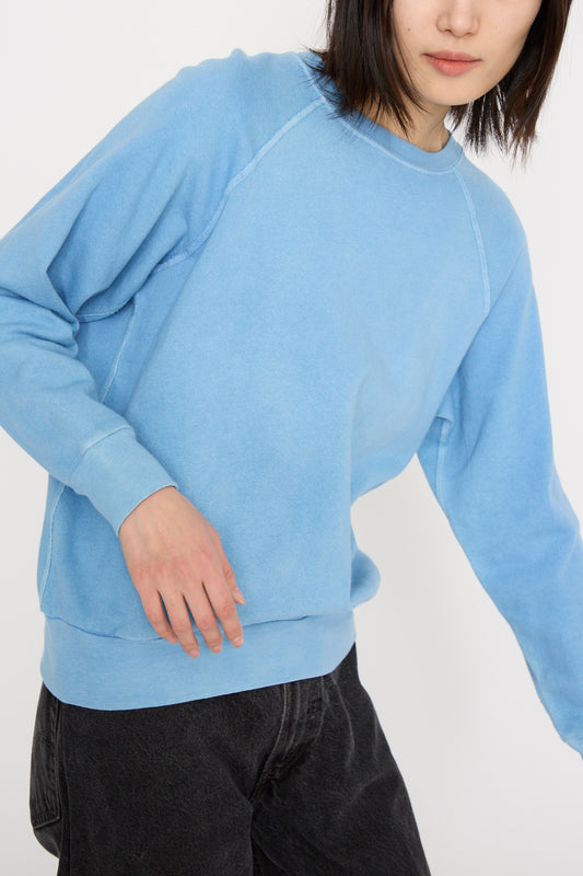 A model wearing the B Sides Crewneck Sweatshirt in Arlo Blue with raglan sleeves and dark pants is partially shown against a plain background.