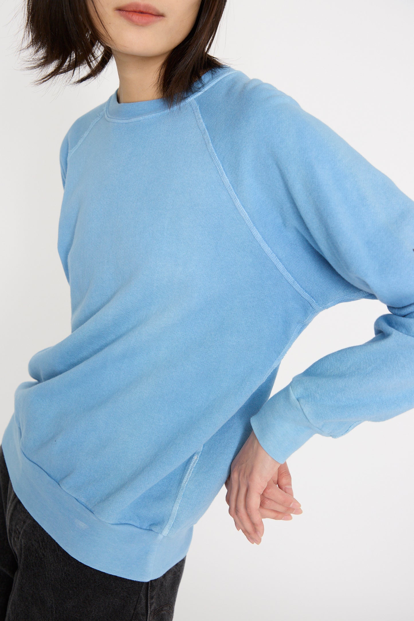 A person wearing the Arlo Blue Crewneck Sweatshirt by B Sides and dark pants poses with hands behind their back against a plain background.