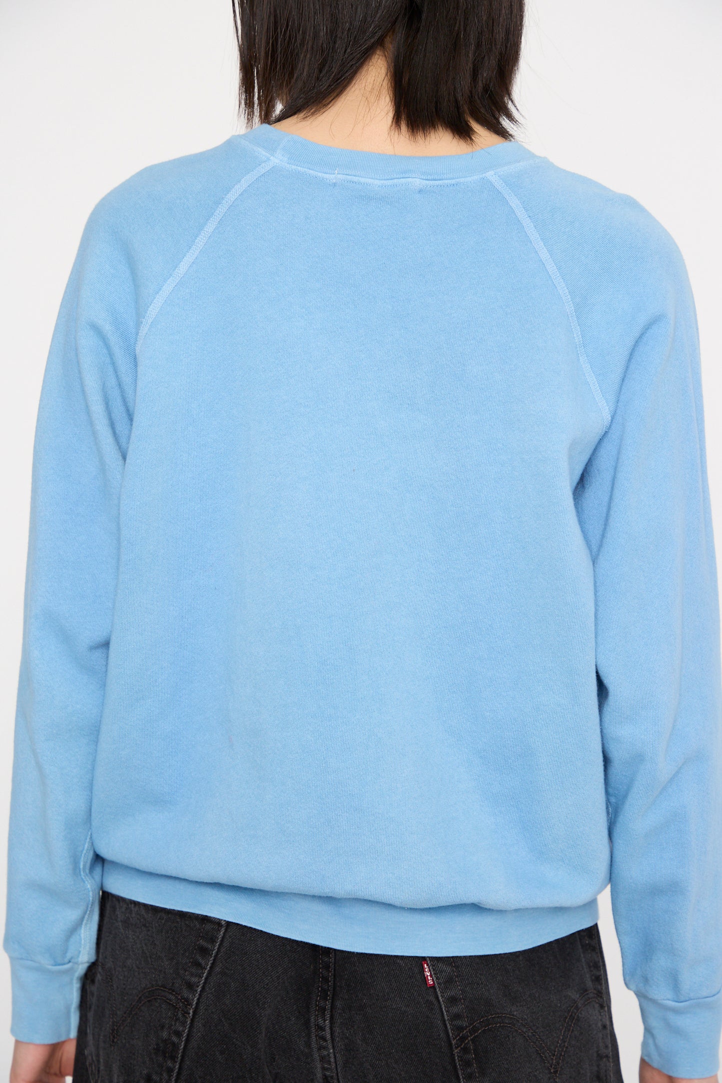 A person is shown from the back wearing B Sides' Crewneck Sweatshirt in Arlo Blue, styled with raglan sleeves, paired with dark jeans.