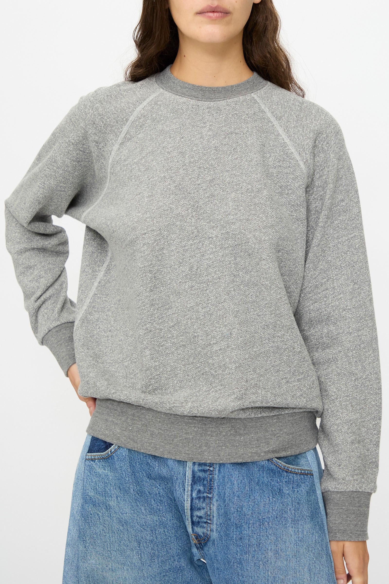 A person wearing the B Sides Crewneck Sweatshirt in Heather Grey and blue jeans stands against a plain white background.
