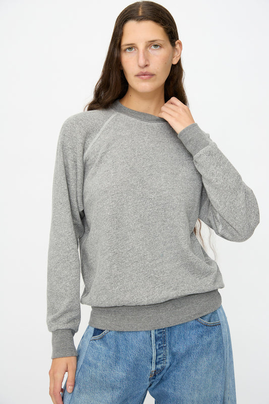 A person with long brown hair wears the B Sides Crewneck Sweatshirt in Heather Grey and blue jeans, standing against a plain white background.