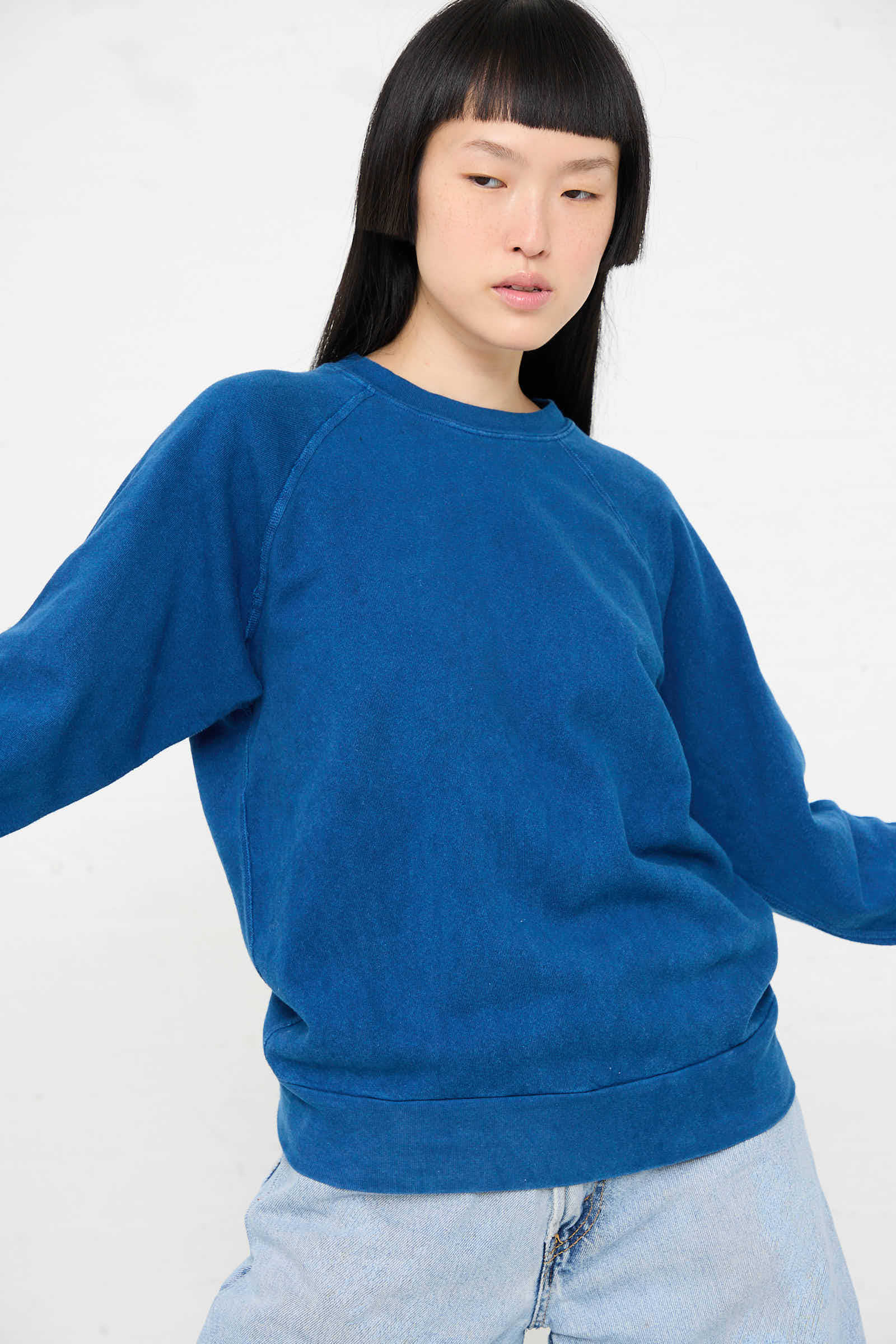 A person wearing the Crewneck Sweatshirt in Van Blue Botanical by B Sides and light blue jeans poses against a plain white background.