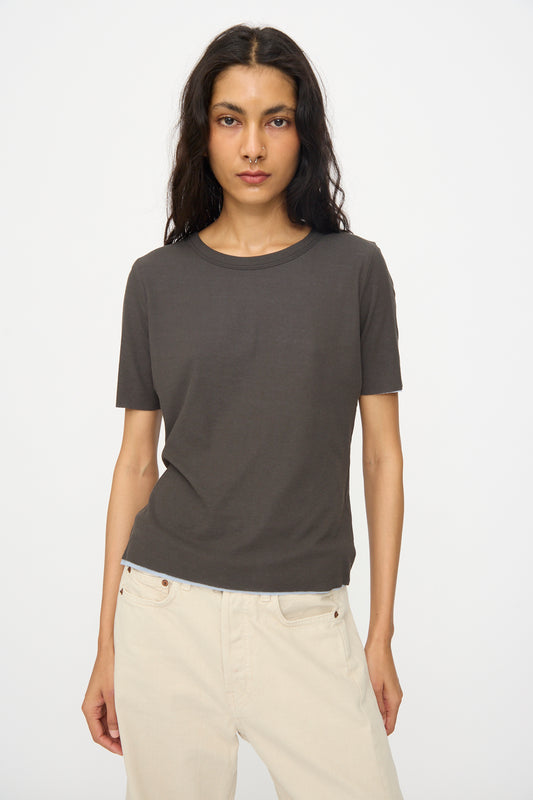 A person wearing the B Sides Double Tee in Dark Grey and Light Blue stands against a plain white background, paired with light beige pants.