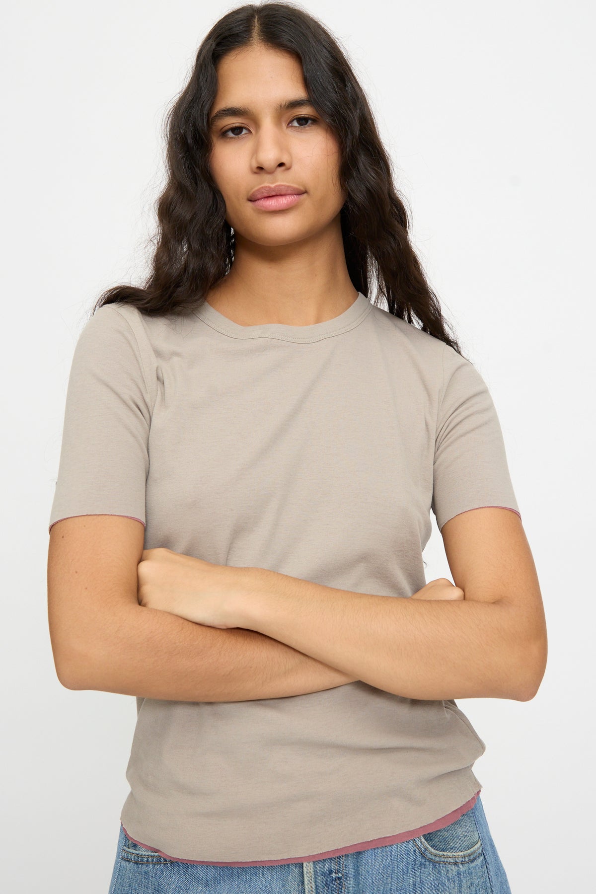 Woman with long brown hair wears the Double Tee in Pink and Dove Grey by B Sides, paired with blue jeans, standing arms crossed against a white background.