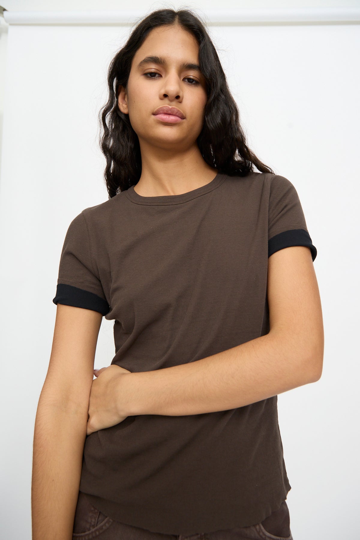 Person with long dark hair wears the Double Tee in Walnut and Black by B Sides, a 100% cotton brown shirt with black trim, standing against a plain white background.