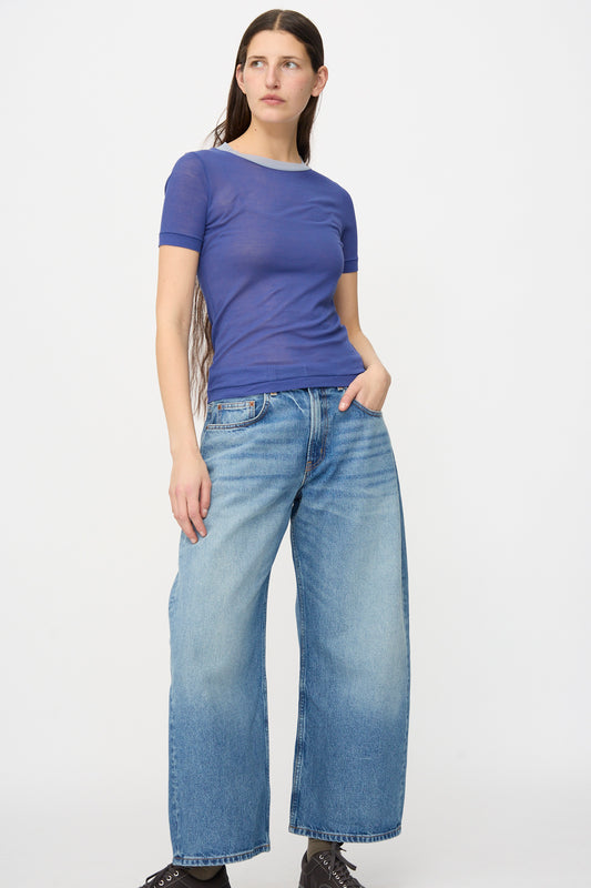 Person stands against a plain background, wearing a fitted blue short-sleeve top and B Sides Floppy Jean in Charley Wash—relaxed fit, wide straight leg—with one hand casually tucked into their pocket.