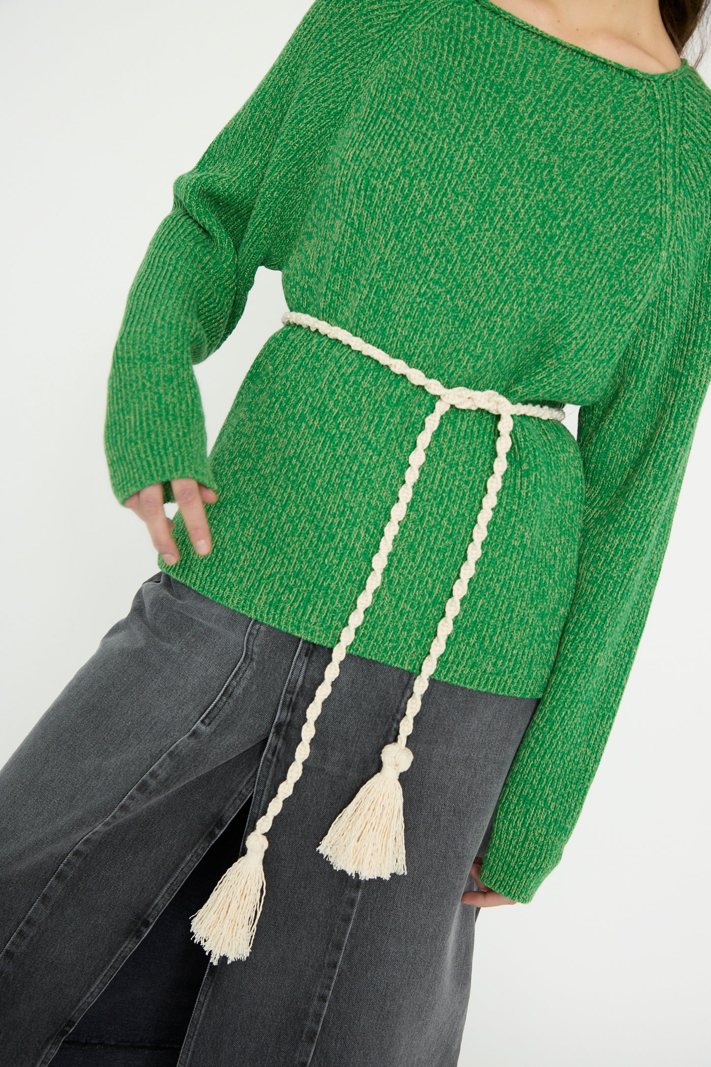 An individual wearing a green sweater with the B Sides Fran Macramé Belt in Ecru and dark pants stands against a light background.