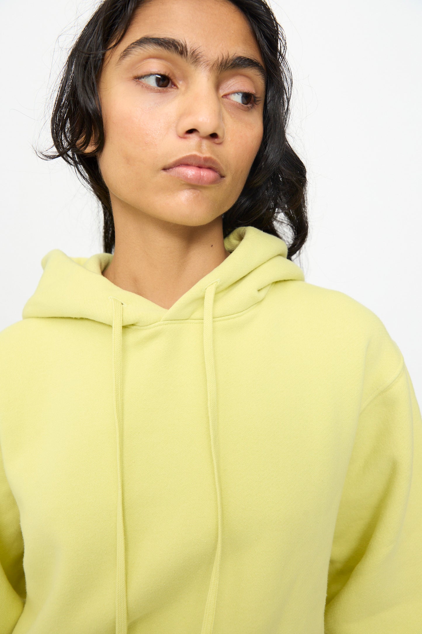 A person wearing the B Sides Hoodie in Celery Overdye with a relaxed fit looks slightly to the side against a plain white background.