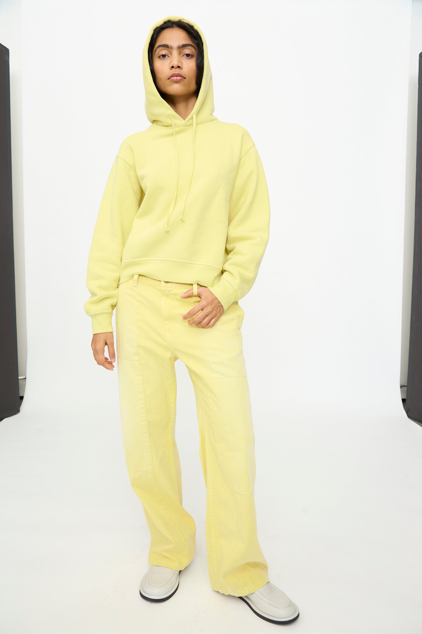 A person stands against a plain white background, hands relaxed at their sides, wearing the B Sides Hoodie in Celery Overdye paired with matching wide-leg pants.