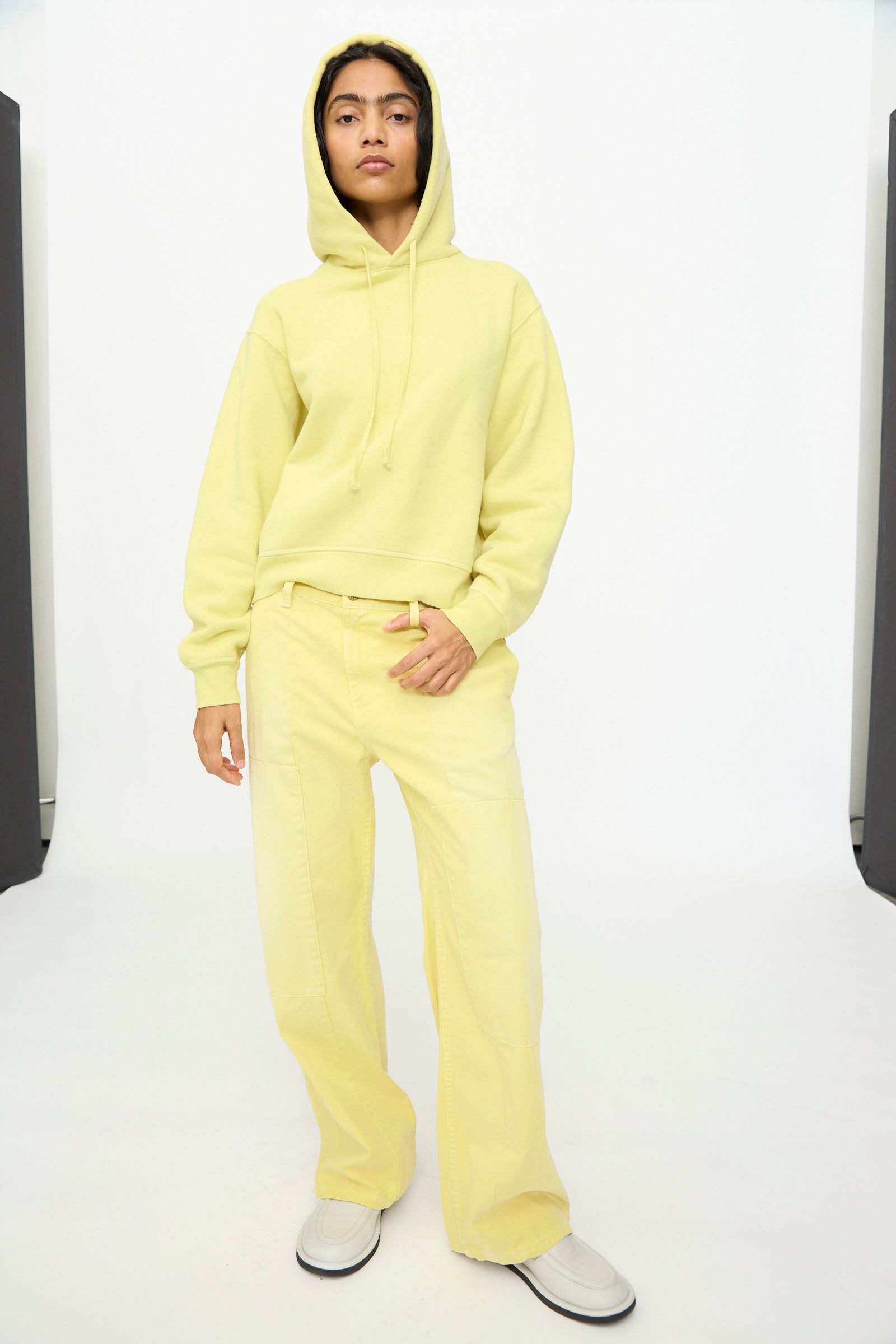A person stands against a plain white background, hands relaxed at their sides, wearing the B Sides Hoodie in Celery Overdye paired with matching wide-leg pants.