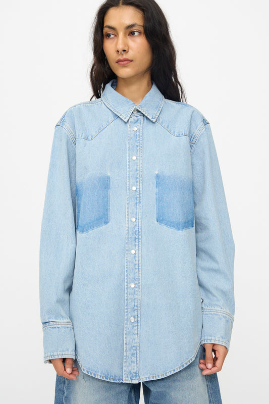 A person wears the B Sides Liv Western Shirt in Park Wash, a relaxed fit light blue denim shirt with two chest pockets, standing against a plain white background.