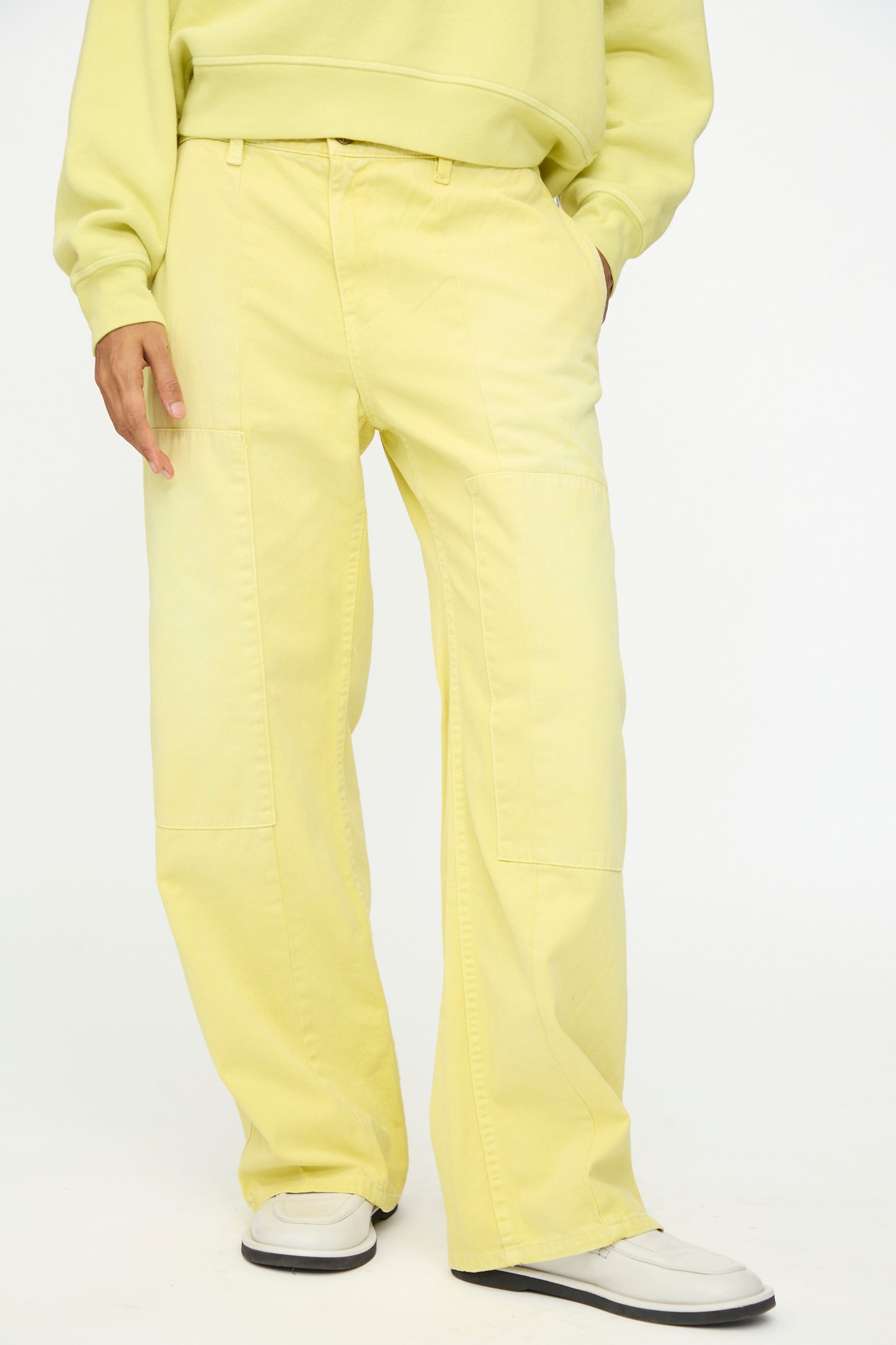 A person wearing B Sides Painter Pant in Faded Celery Overdye stands against a plain background, paired with a matching sweatshirt and white shoes.