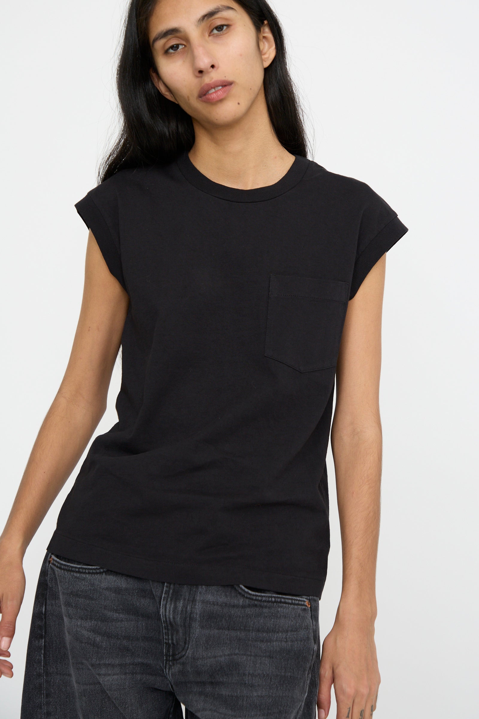 A person with long dark hair is wearing the B Sides Pocket Tank in Stil Black and dark pants against a neutral background.