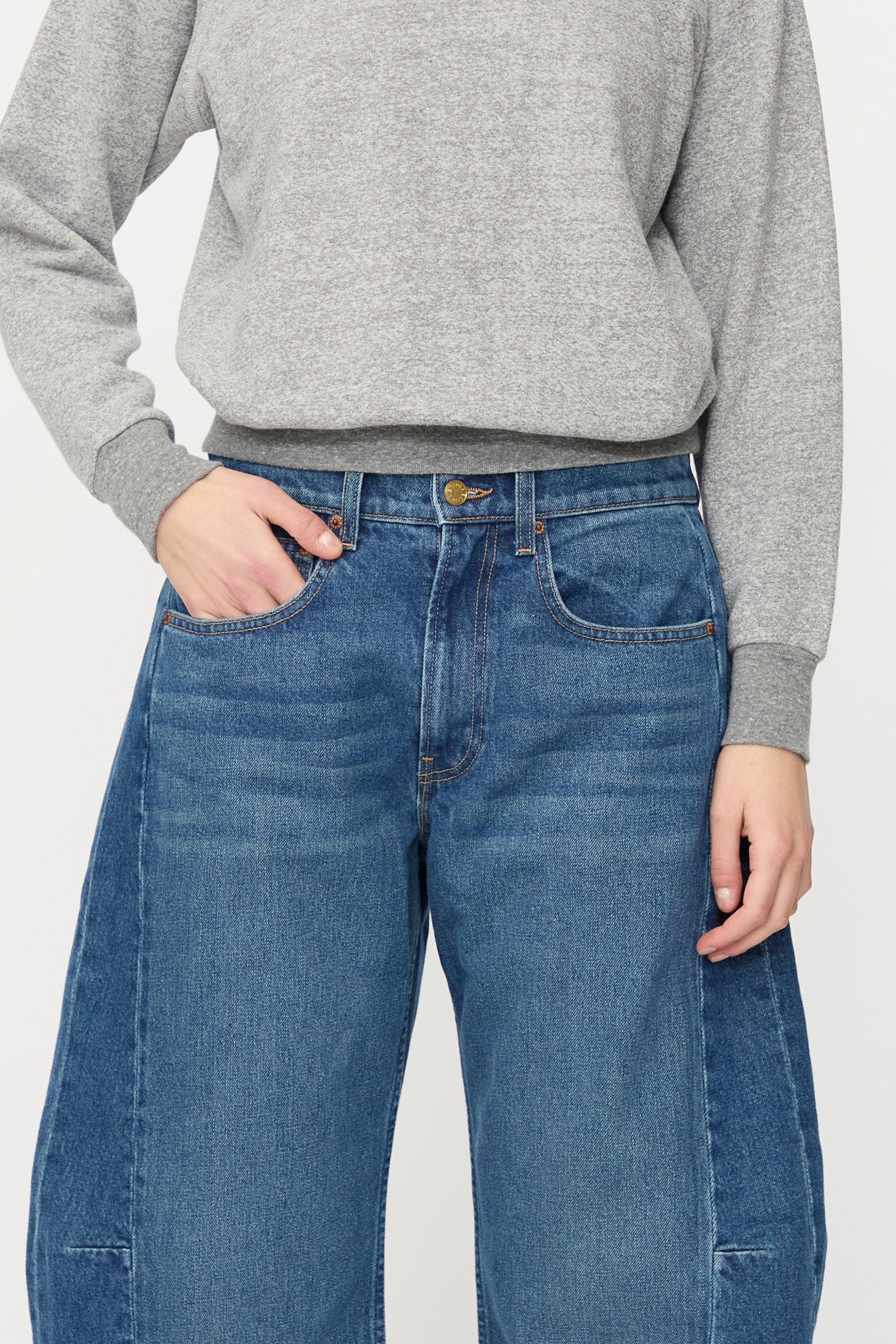 Model wearing a light gray long-sleeve shirt and B Sides Relaxed Cuffed Lasso Jean in Cate Wash, with one hand in their pocket. Shown from shoulders to mid-thigh.