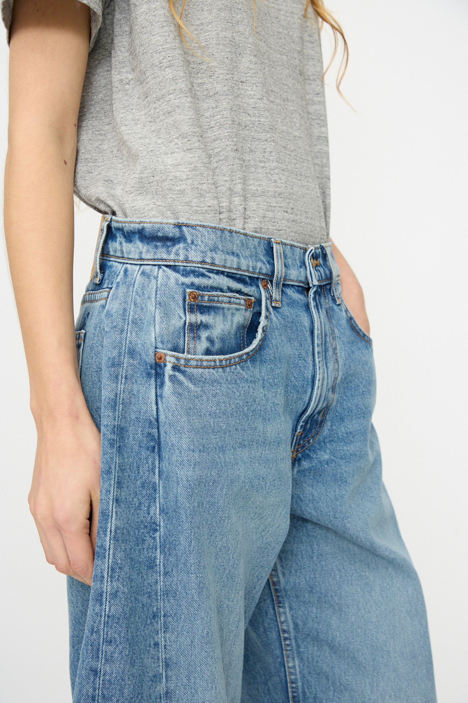 A person wears a loose grey t-shirt and B Sides Relaxed Cuffed Lasso Jean in Jane Wash, with one hand in their pocket, shown from shoulder to mid-thigh against a plain background.